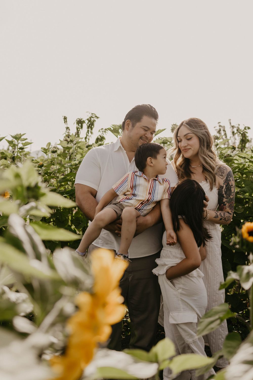 A family shares a tender moment together in a sunlit garden surrounded by green foliage and yellow flowers.