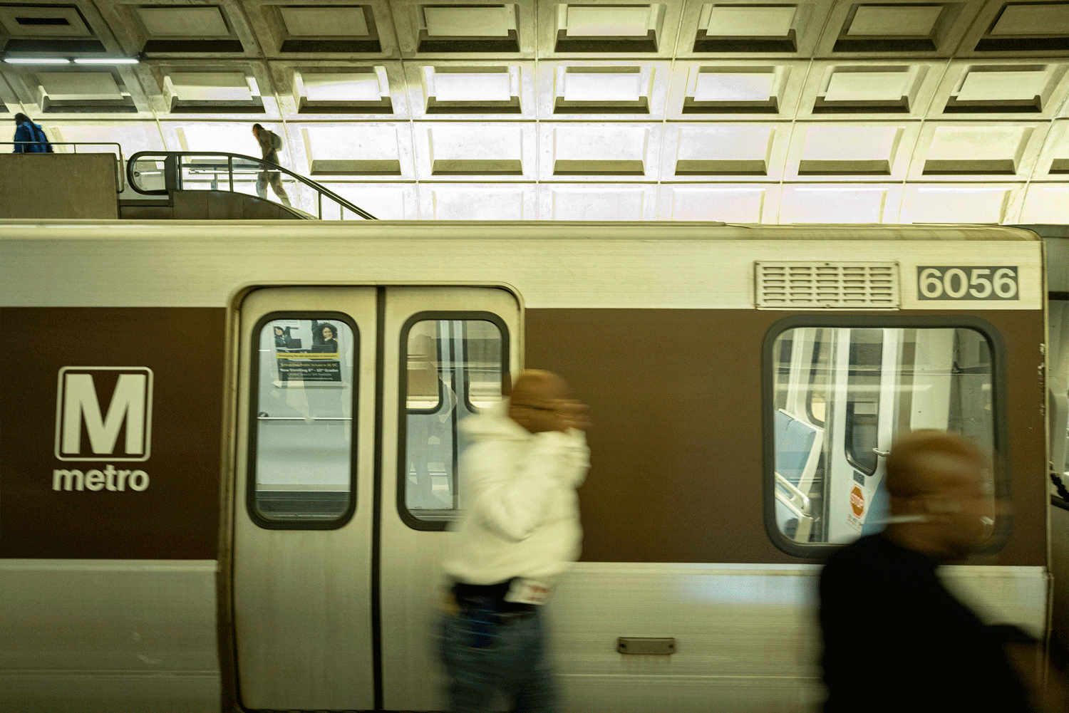 Motion blur of passengers boarding a Metro train car with number 6054 visible at a station platform.