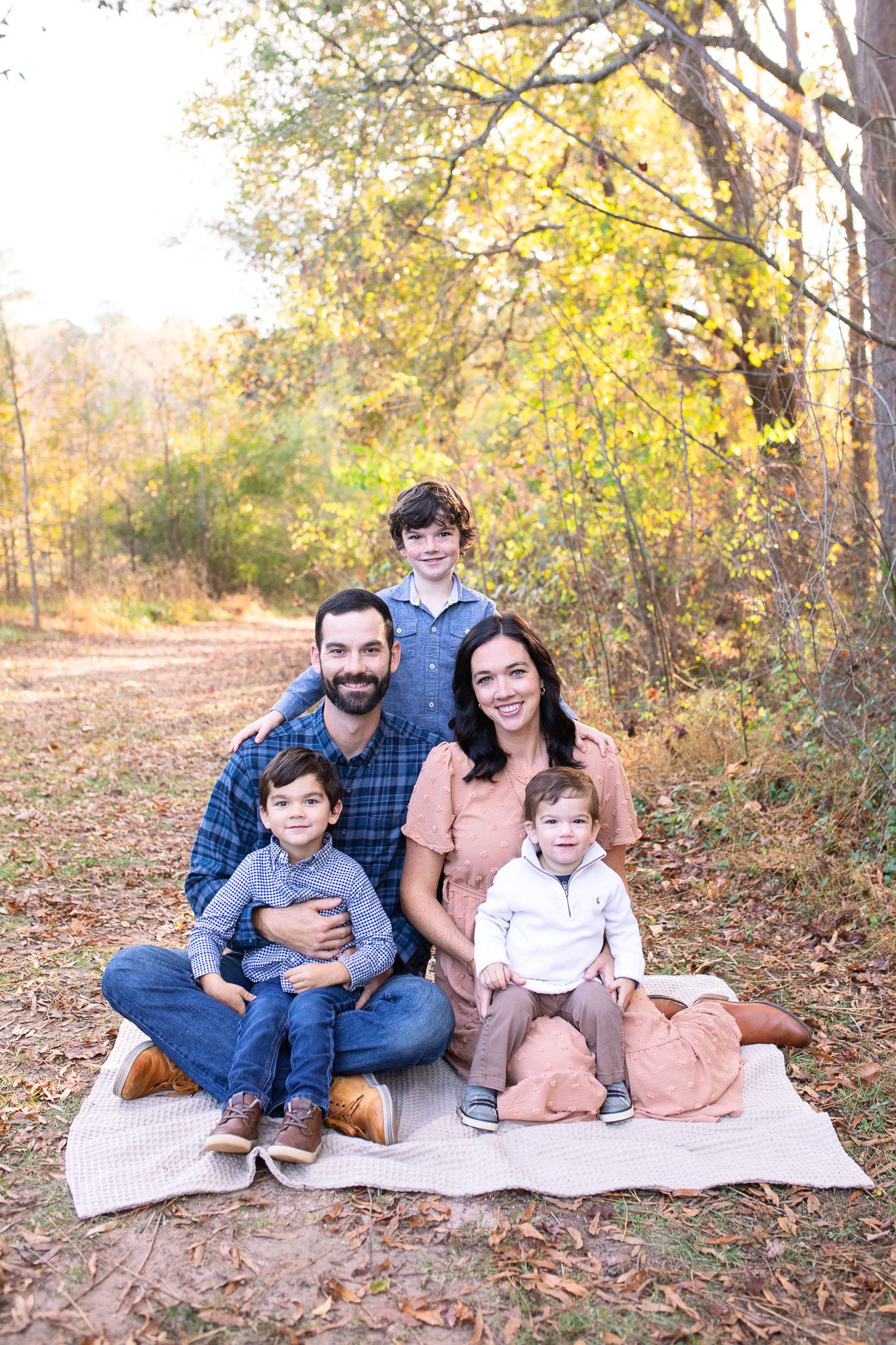 Family sitting together on blanket during autumn photoshoot with colorful fall foliage in background at Sugg Farm