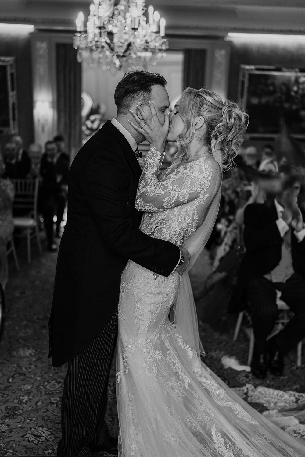 A romantic black and white photo of newlyweds sharing their first dance under a crystal chandelier.