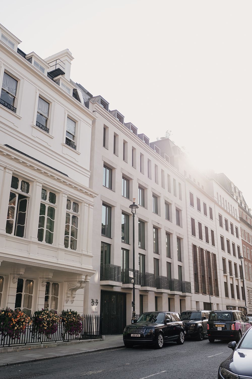 Sunlit white Georgian townhouses with black cars parked along a London street.