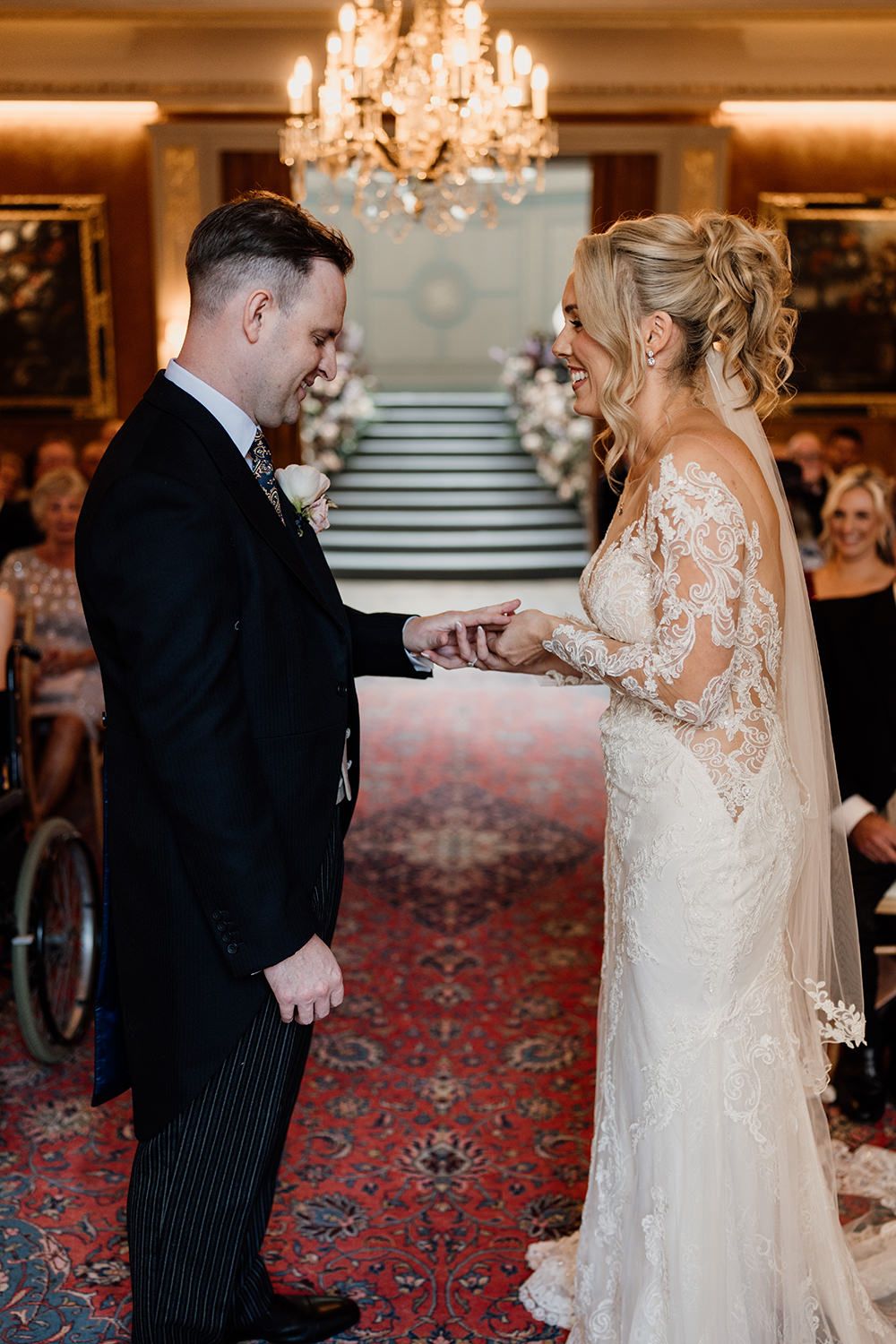 A couple shares an intimate moment during their wedding ceremony in an elegant room with a chandelier.