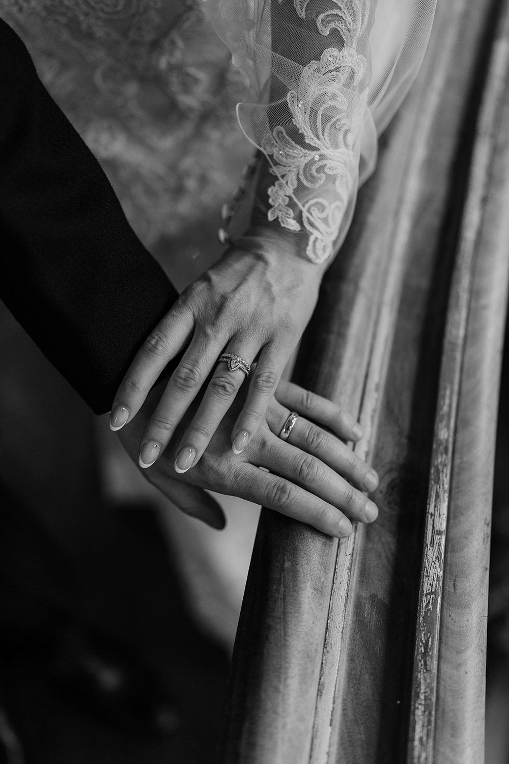 Black and white close-up of hands showing wedding rings and lace sleeve detail.