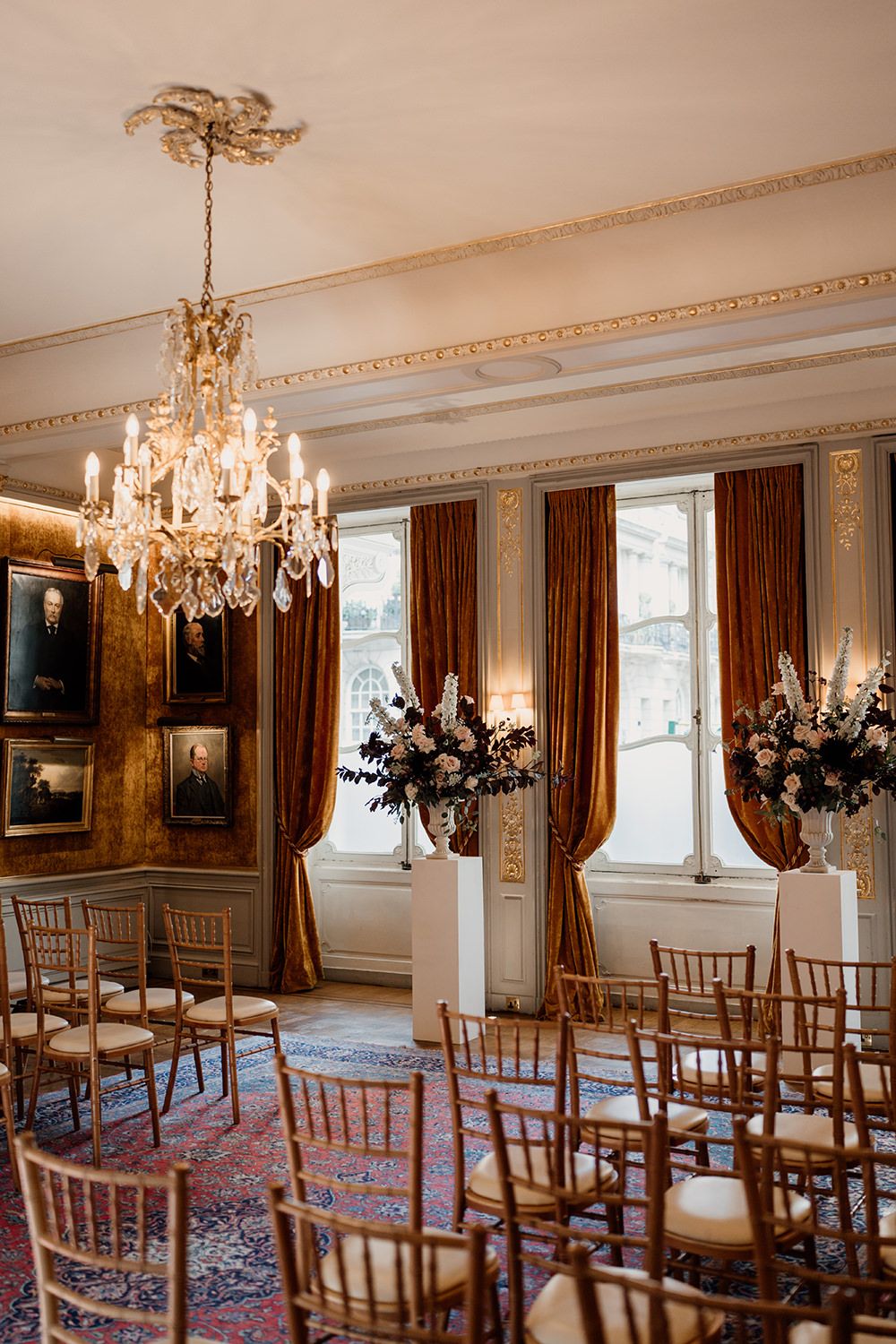 Elegant ballroom with crystal chandelier, gold chairs and rich burgundy drapes set up for an intimate wedding ceremony.