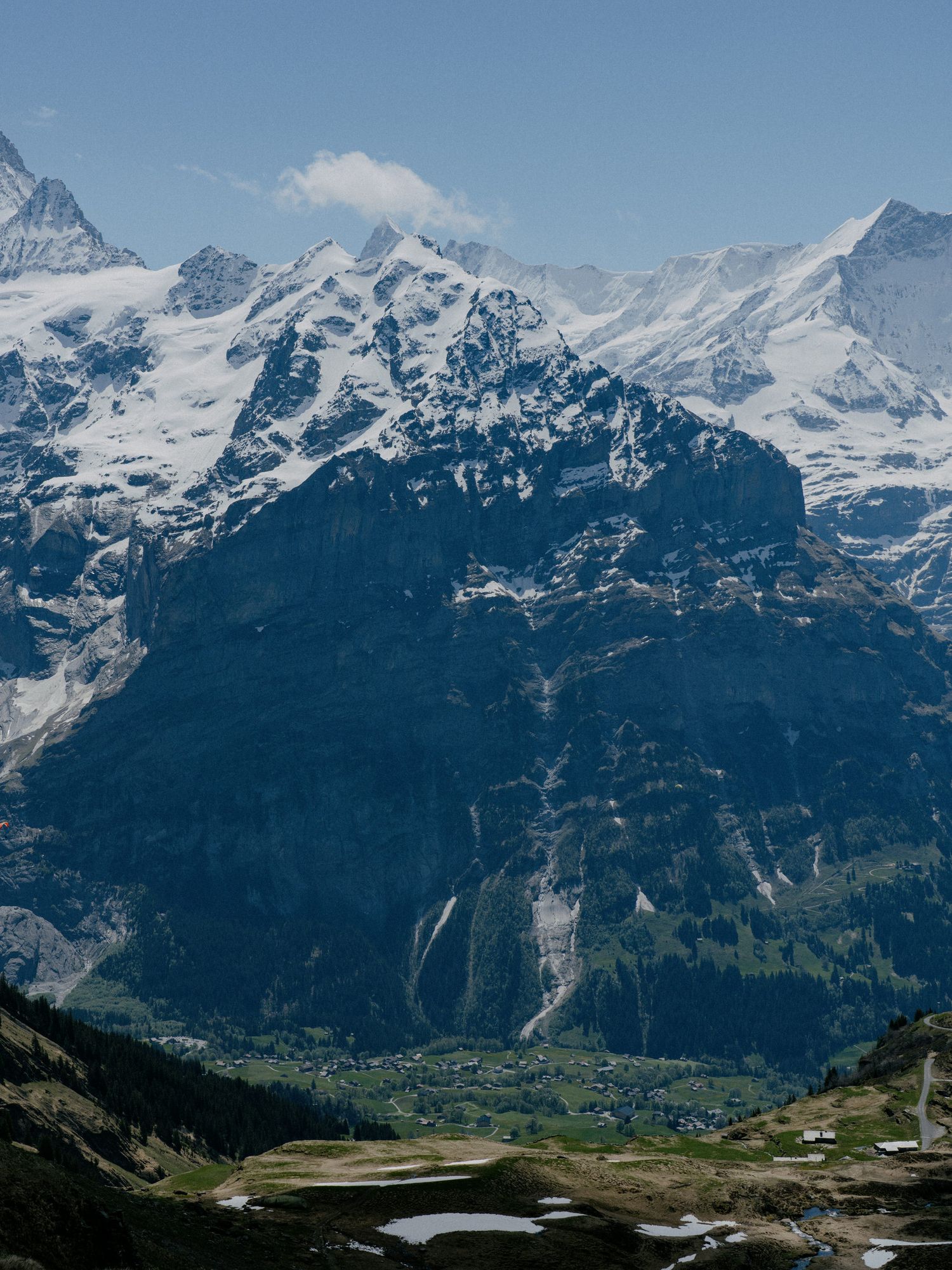 Snow-capped Alpine mountains tower over a small village with dramatic waterfalls cascading down steep cliffs in Switzerland.