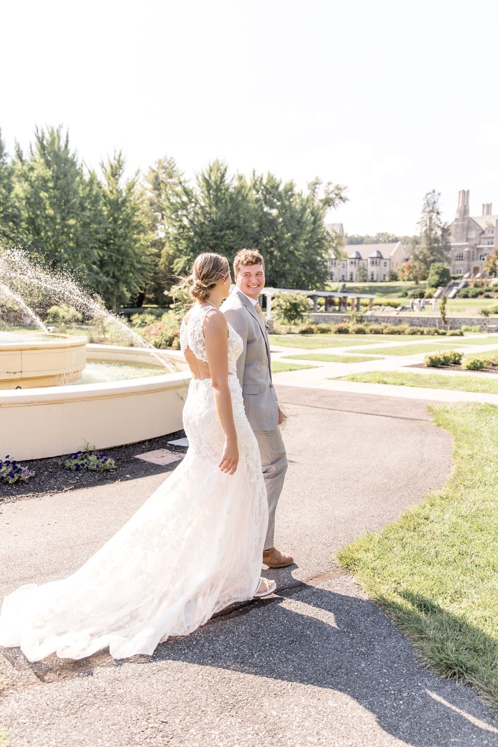 Wedding couple walking down a curved path in elegant attire with flowing dress and natural scenery.