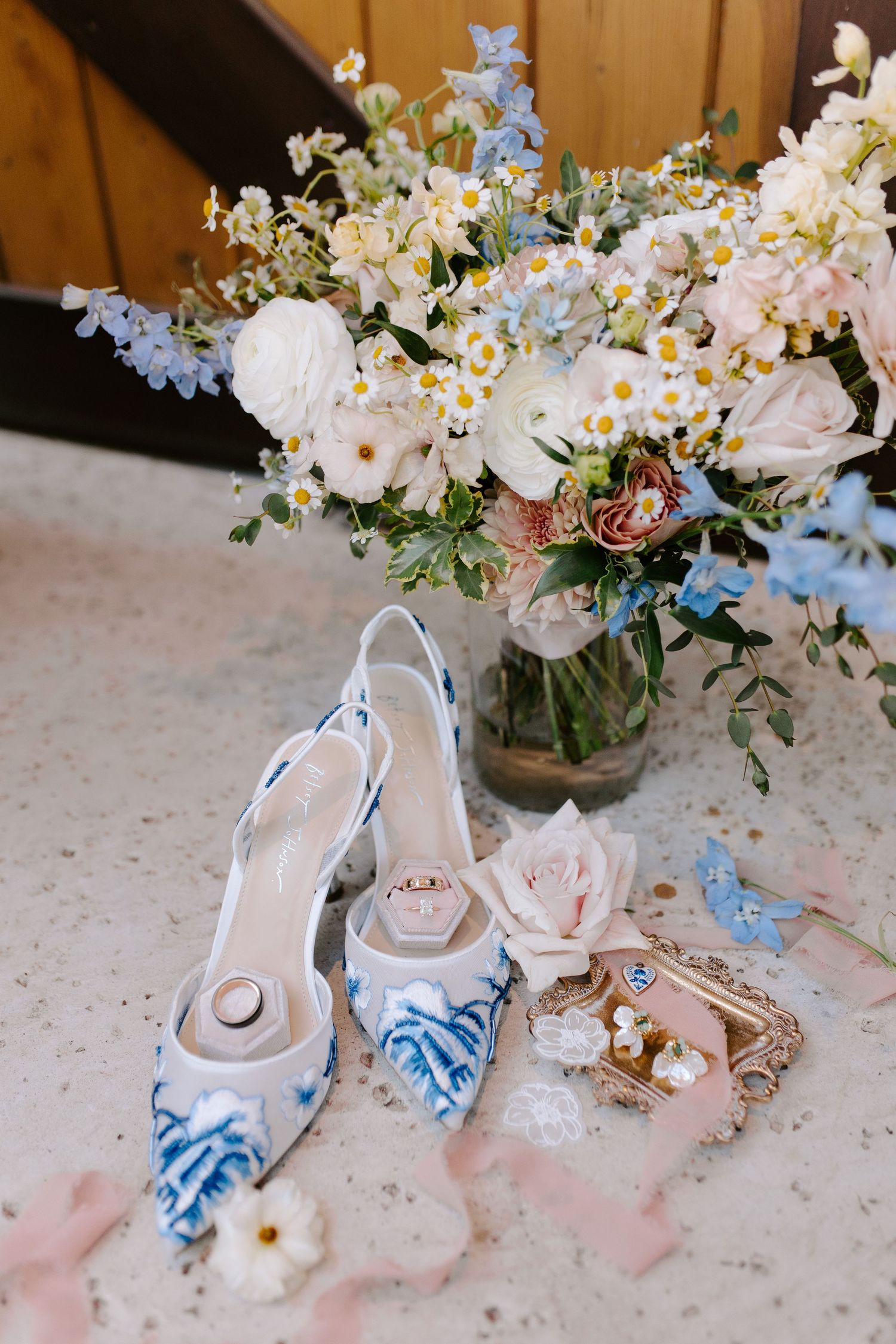 Elegant white bridal shoes with blue floral details displayed alongside delicate flower arrangements.