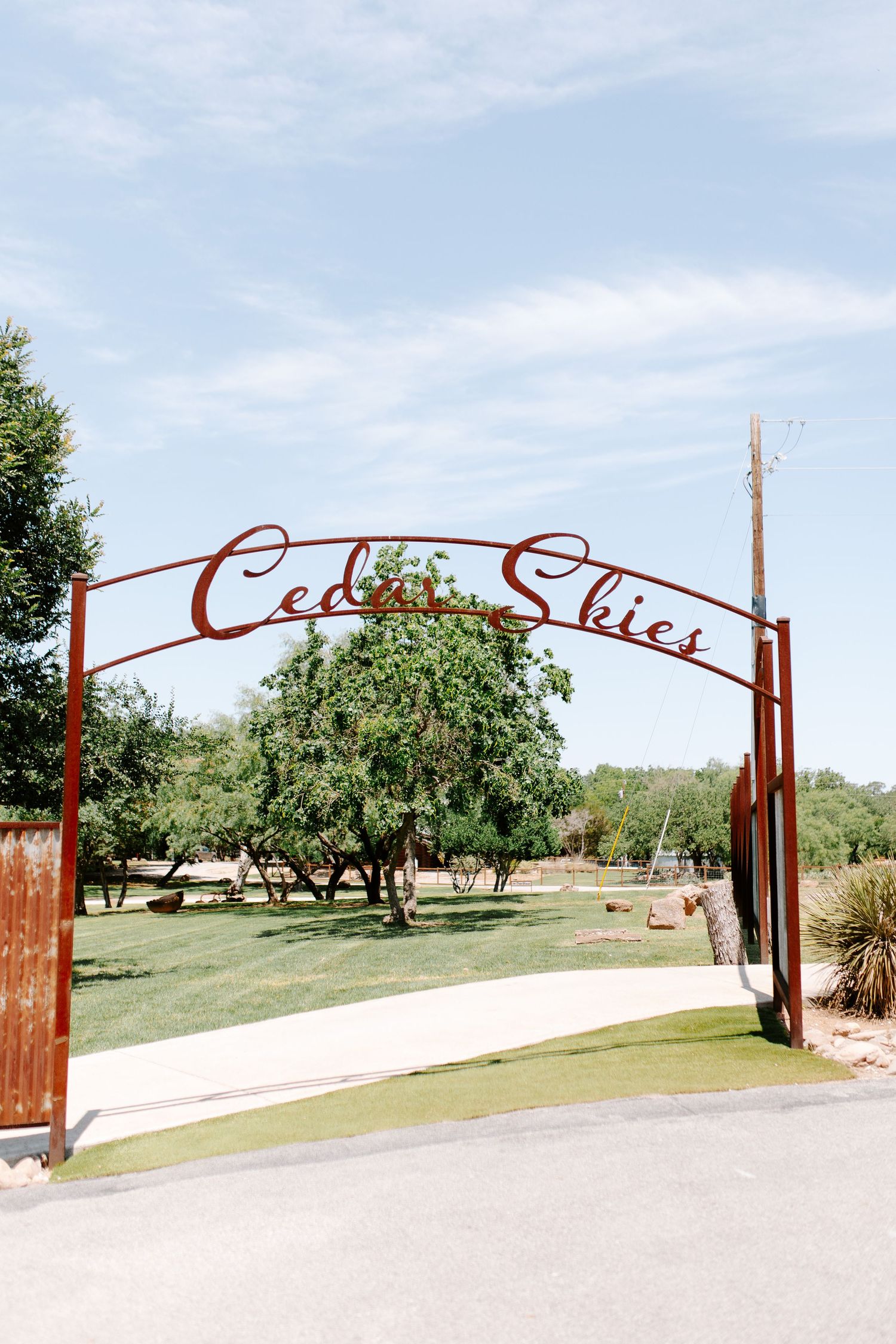 Rustic metal entrance gate with cursive lettering spans across a country driveway.