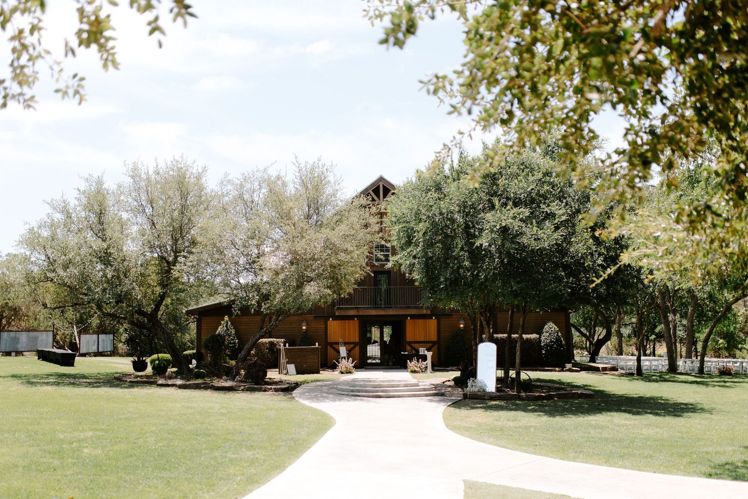 A rustic wooden wedding venue with a barn-style building nestled among trees on a grassy lawn.
