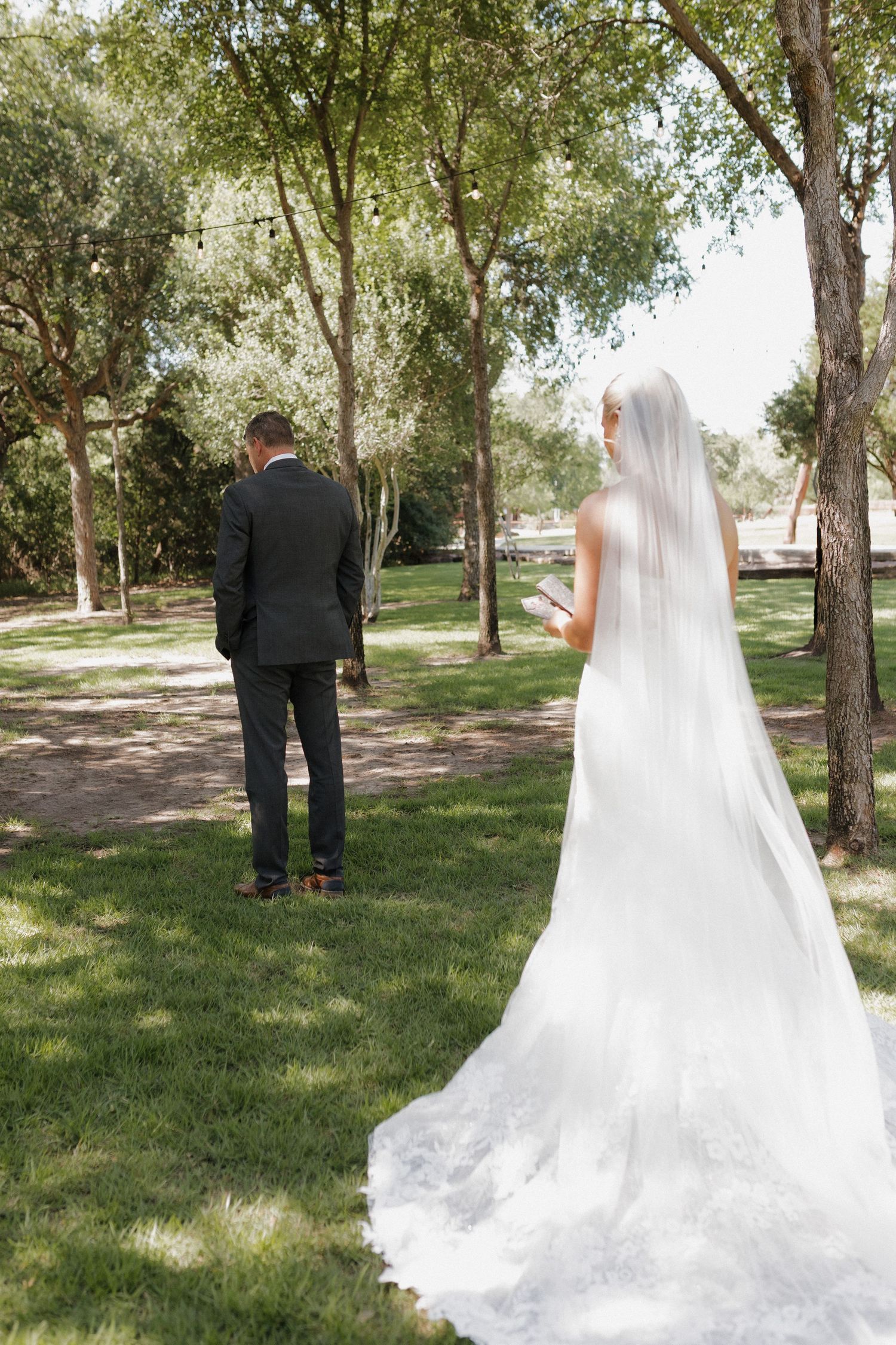 A first look wedding moment captured from behind in a sunny garden setting.