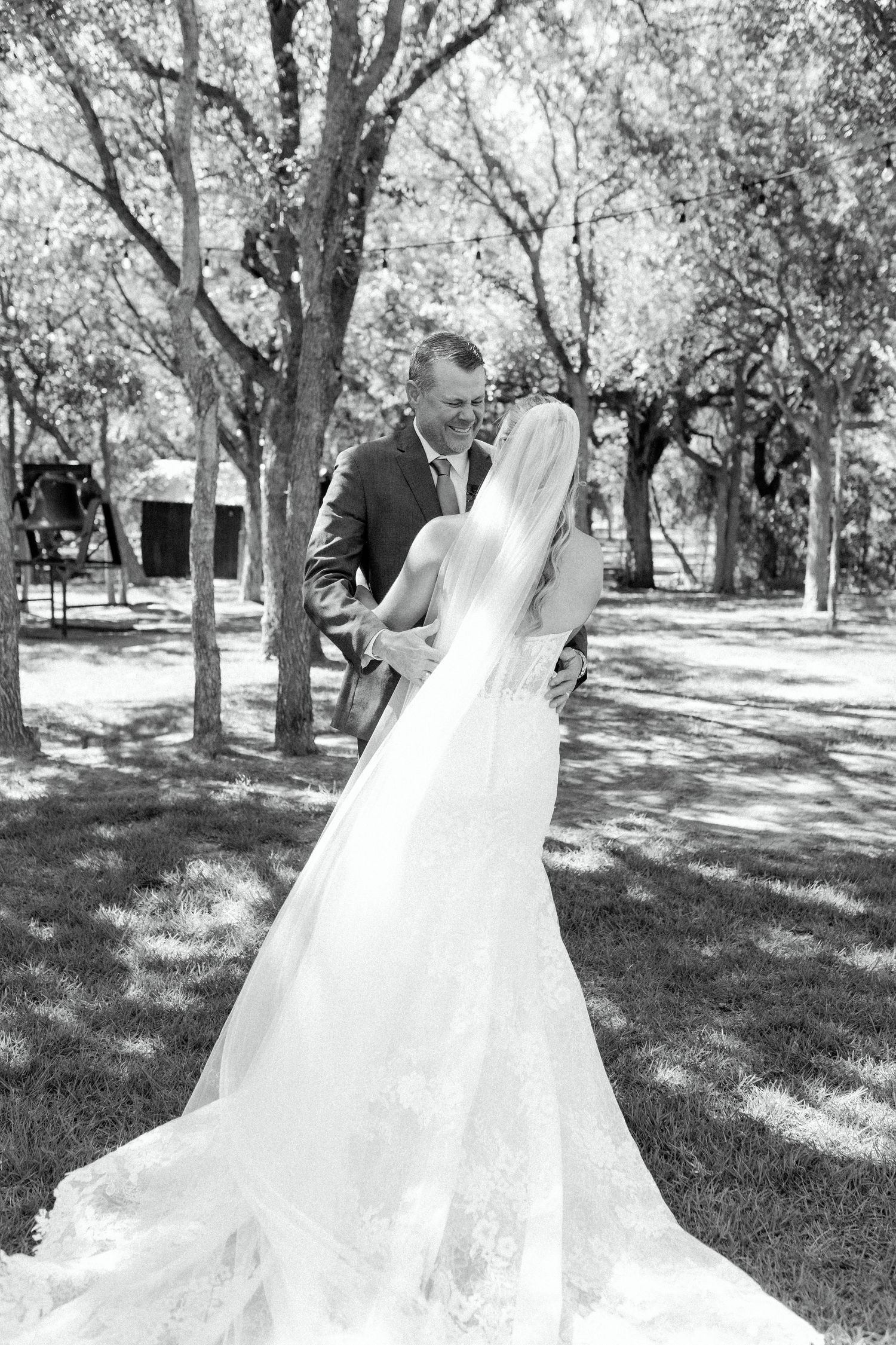 Flowing white wedding gown with long train captured in sunlit outdoor setting among trees.