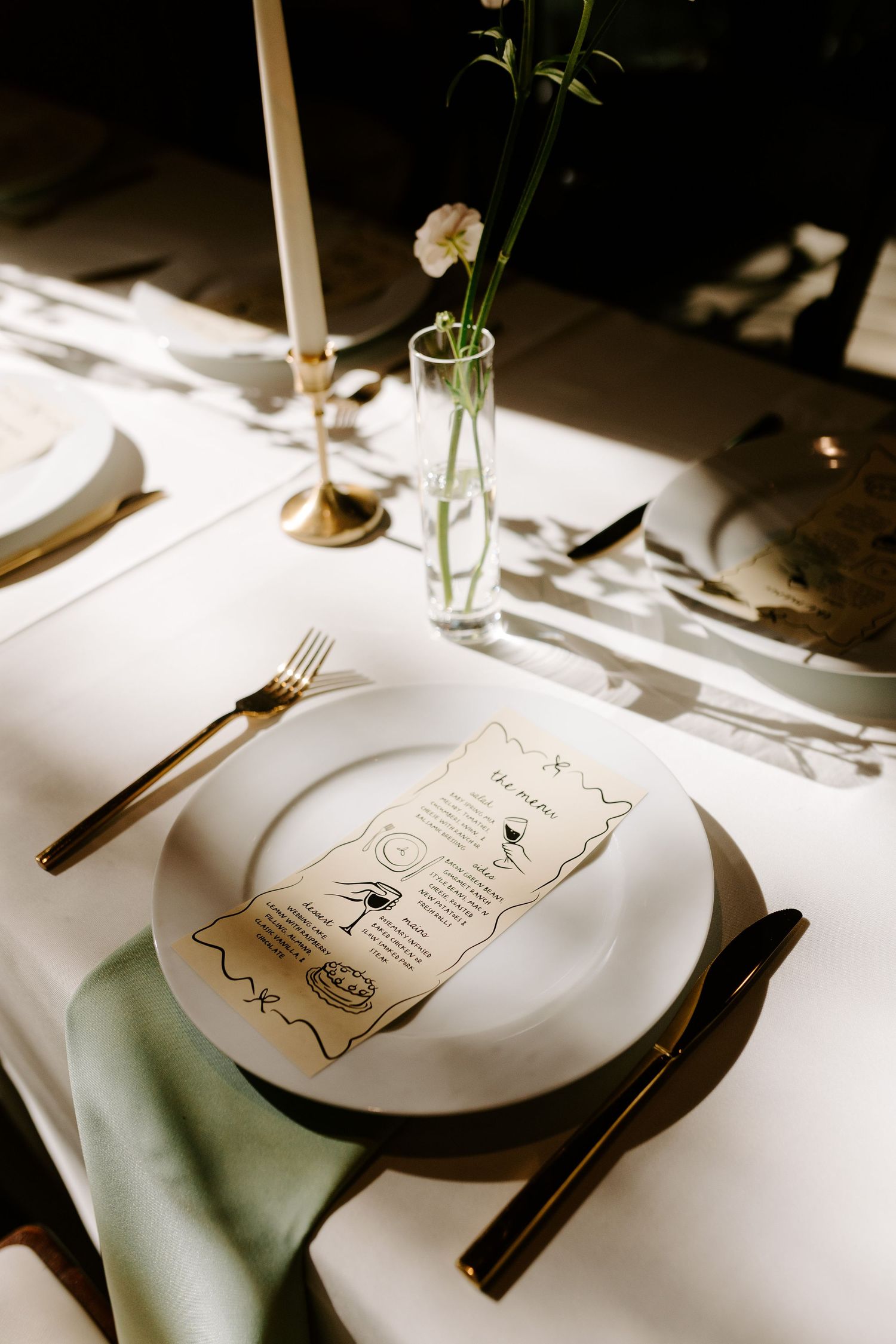 An elegant place setting with white plates, gold cutlery and a single flower in a vase.