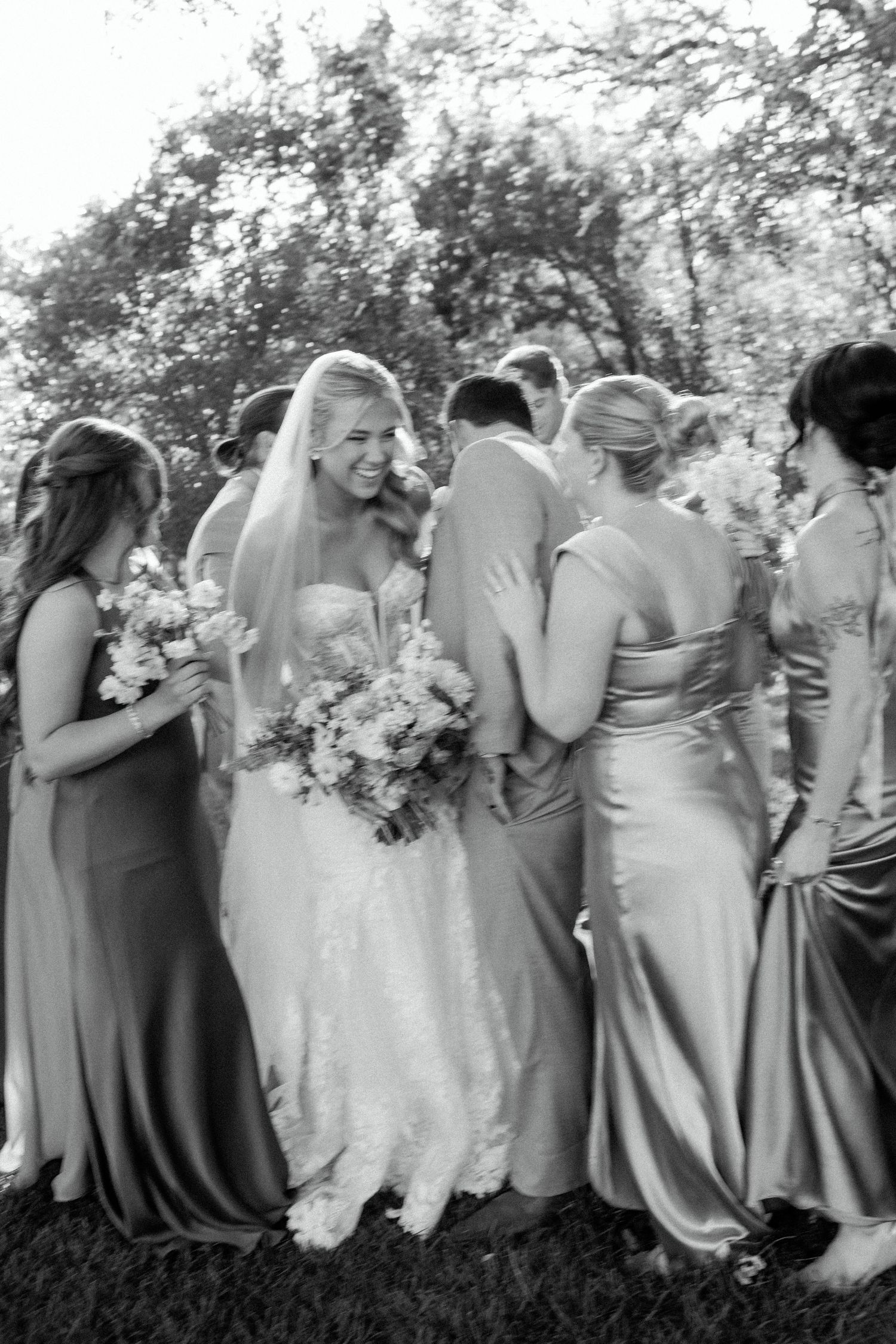 Wedding party in formal attire gathered outdoors for black and white photography.