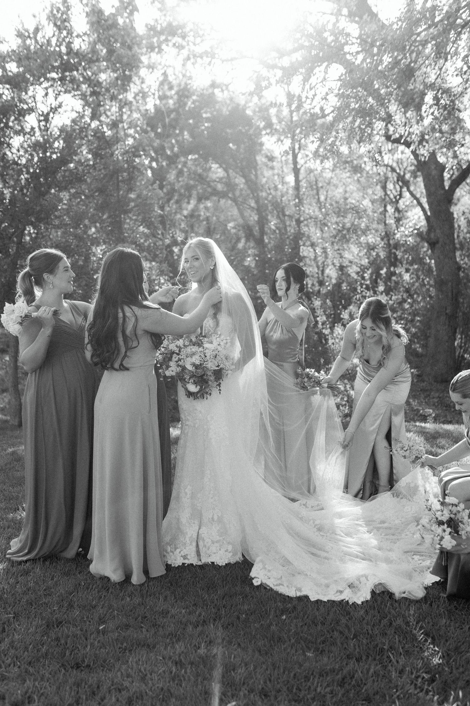 Black and white photo capturing candid moments between bridal party members in an outdoor garden setting.