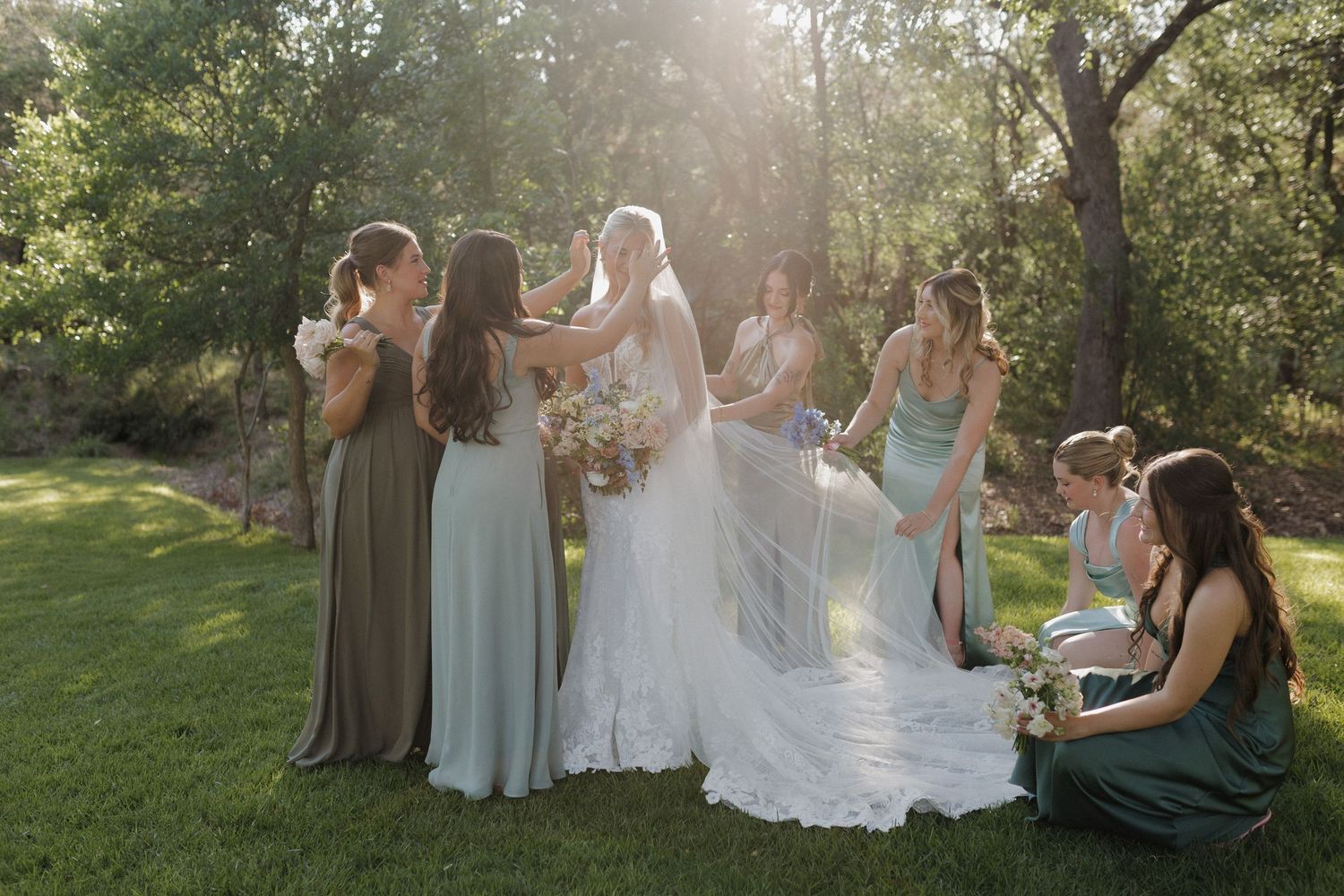 A sunlit gathering of wedding attendants in flowing dresses during an outdoor celebration.