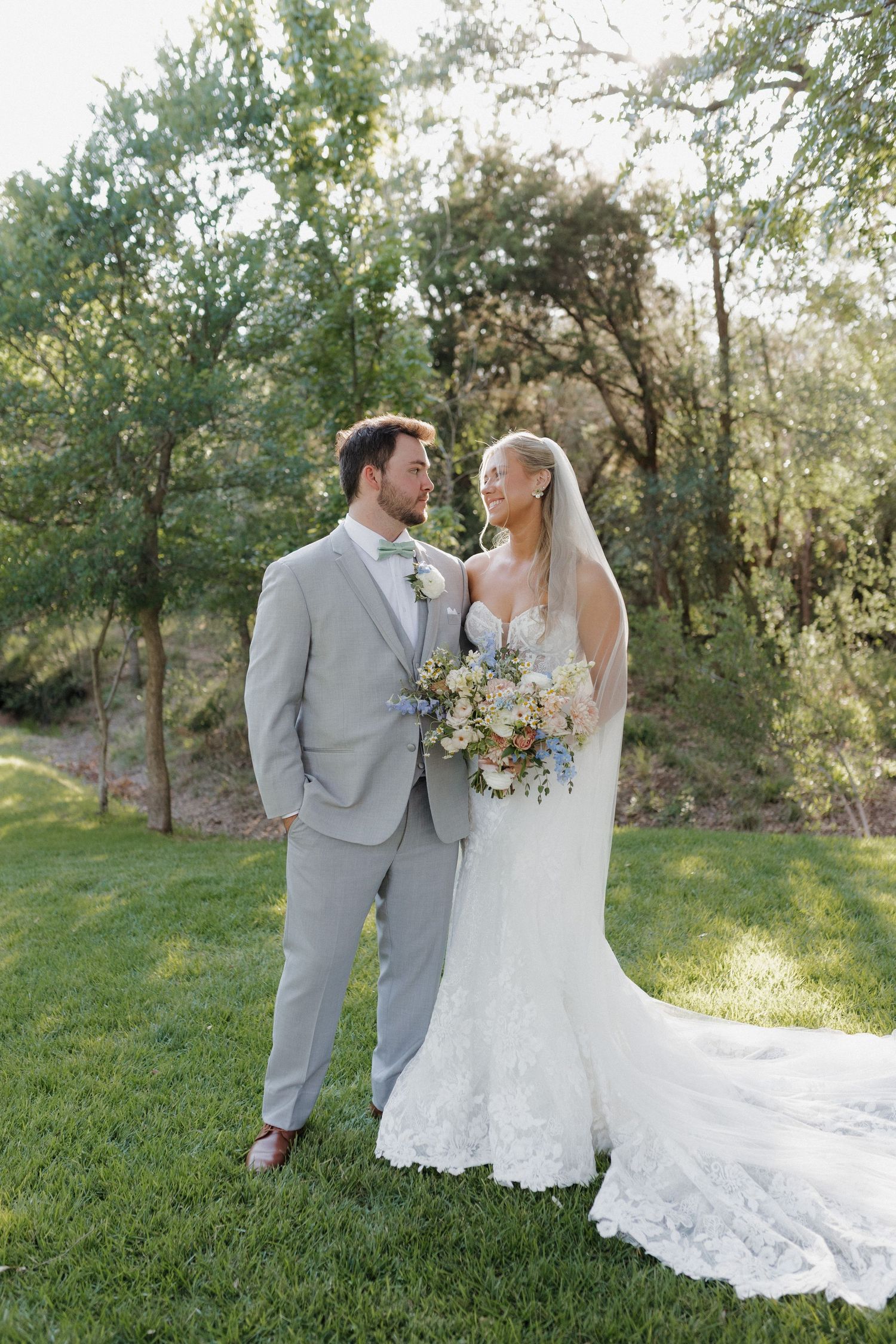 A romantic wedding portrait of a couple in a lush garden setting with the bride holding a delicate floral bouquet.