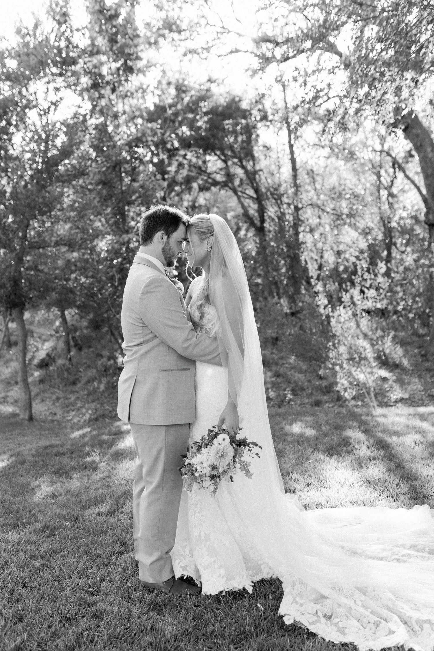 Black and white romantic wedding portrait of a couple embracing in a natural outdoor setting.