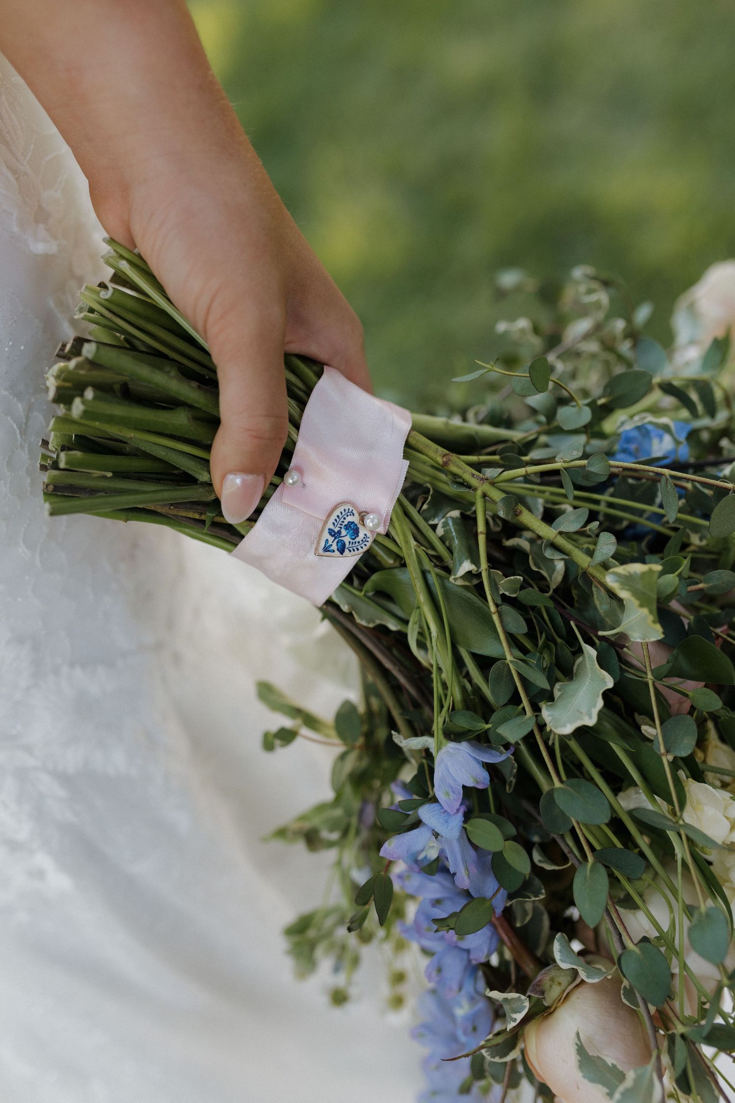 A close-up of a wedding bouquet with blue flowers and greenery wrapped in a commemorative ribbon.