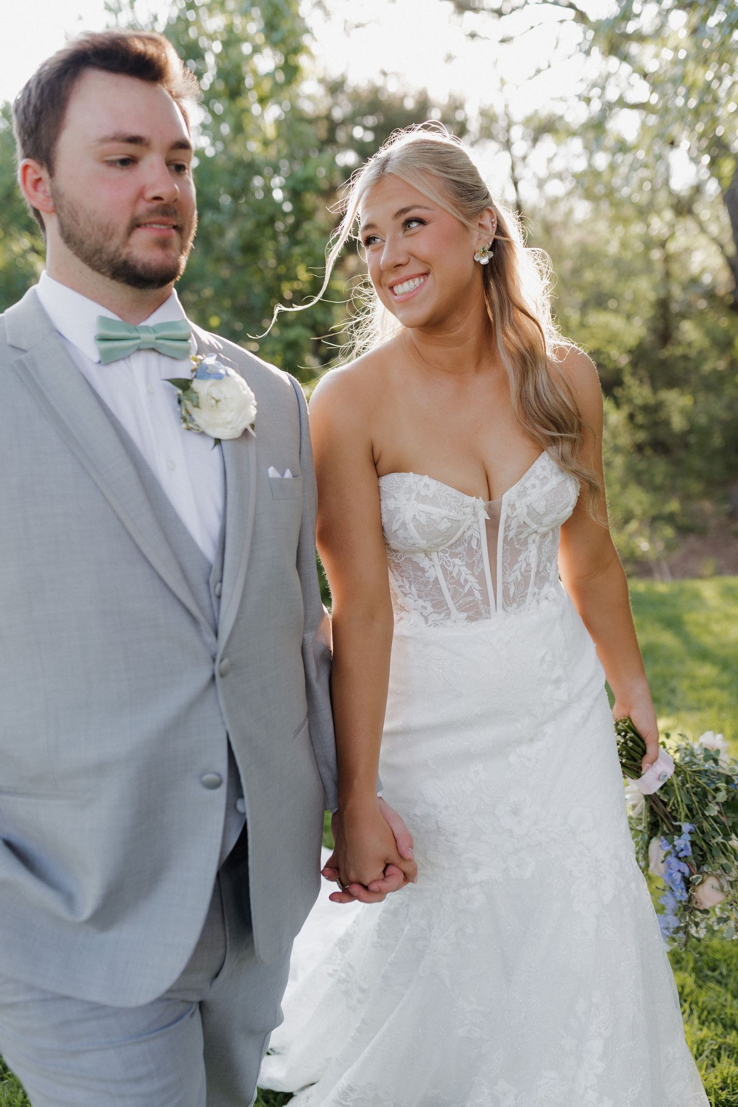 A couple shares a happy moment together outdoors during their wedding in light grey and white attire.