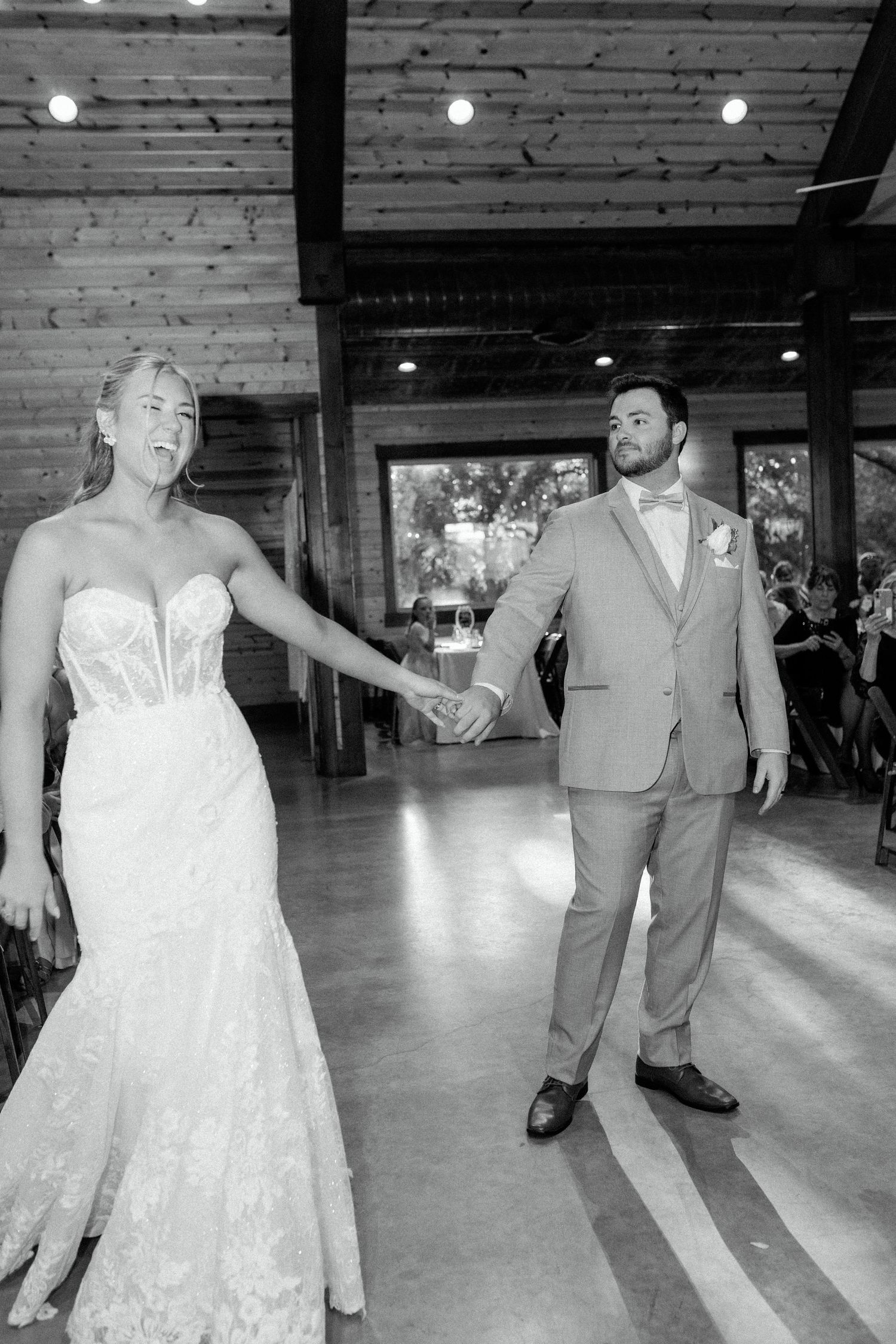 A couple shares their first dance in a rustic wood-paneled reception venue with overhead lighting.