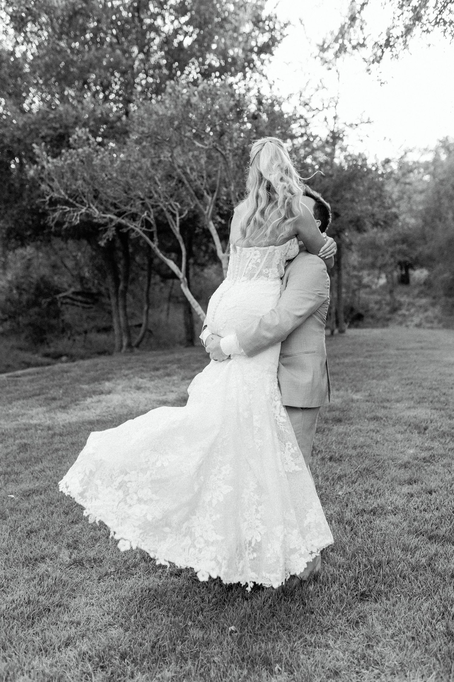 A romantic black and white photo shows a couple embracing outdoors, with the bride wearing a stunning lace mermaid gown.