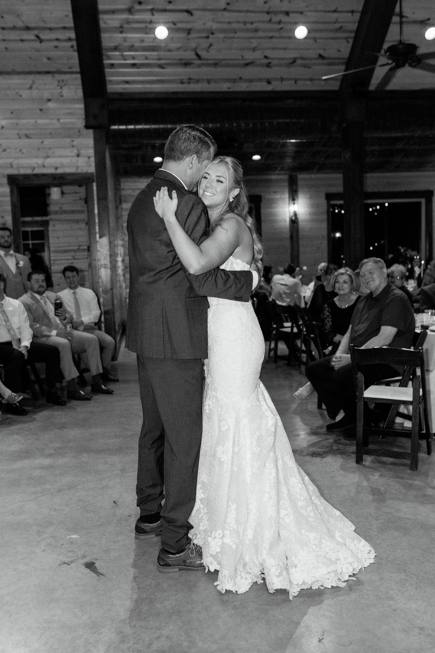 A couple shares their first dance at a rustic indoor wedding venue with exposed beams and brick walls.