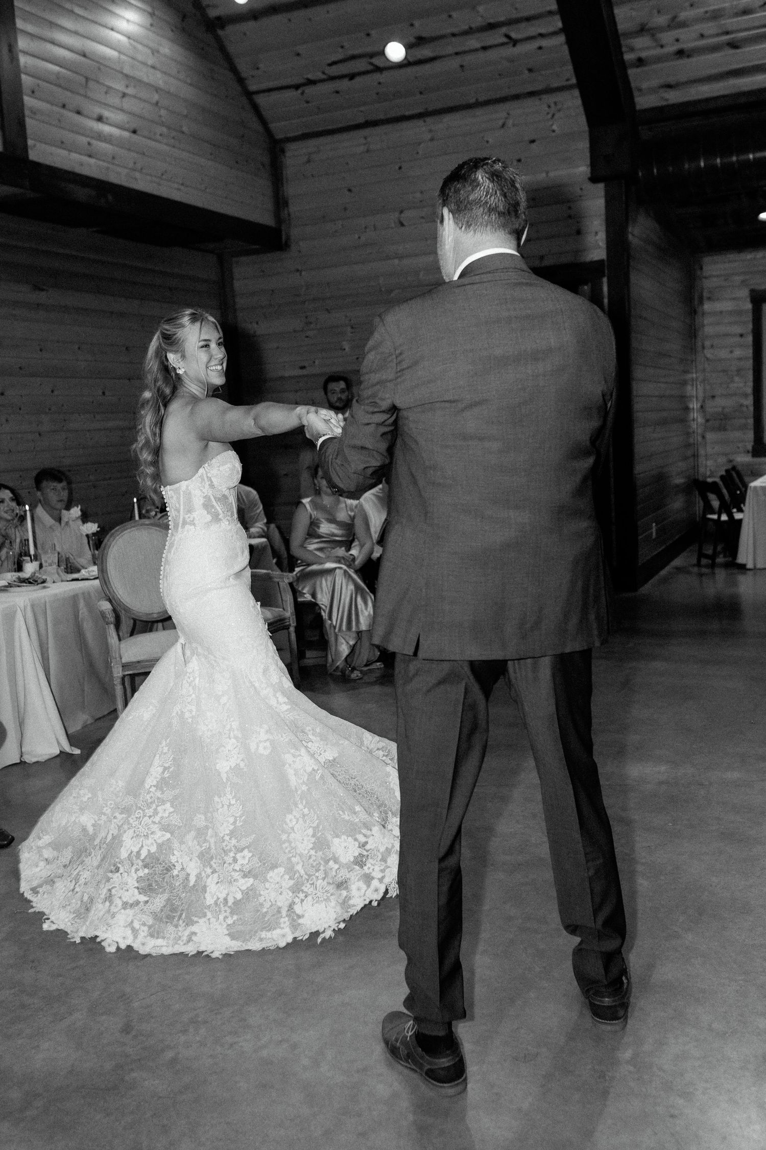 Elegant wedding reception dance shows a bride in a lace gown twirling in a rustic venue with brick walls.