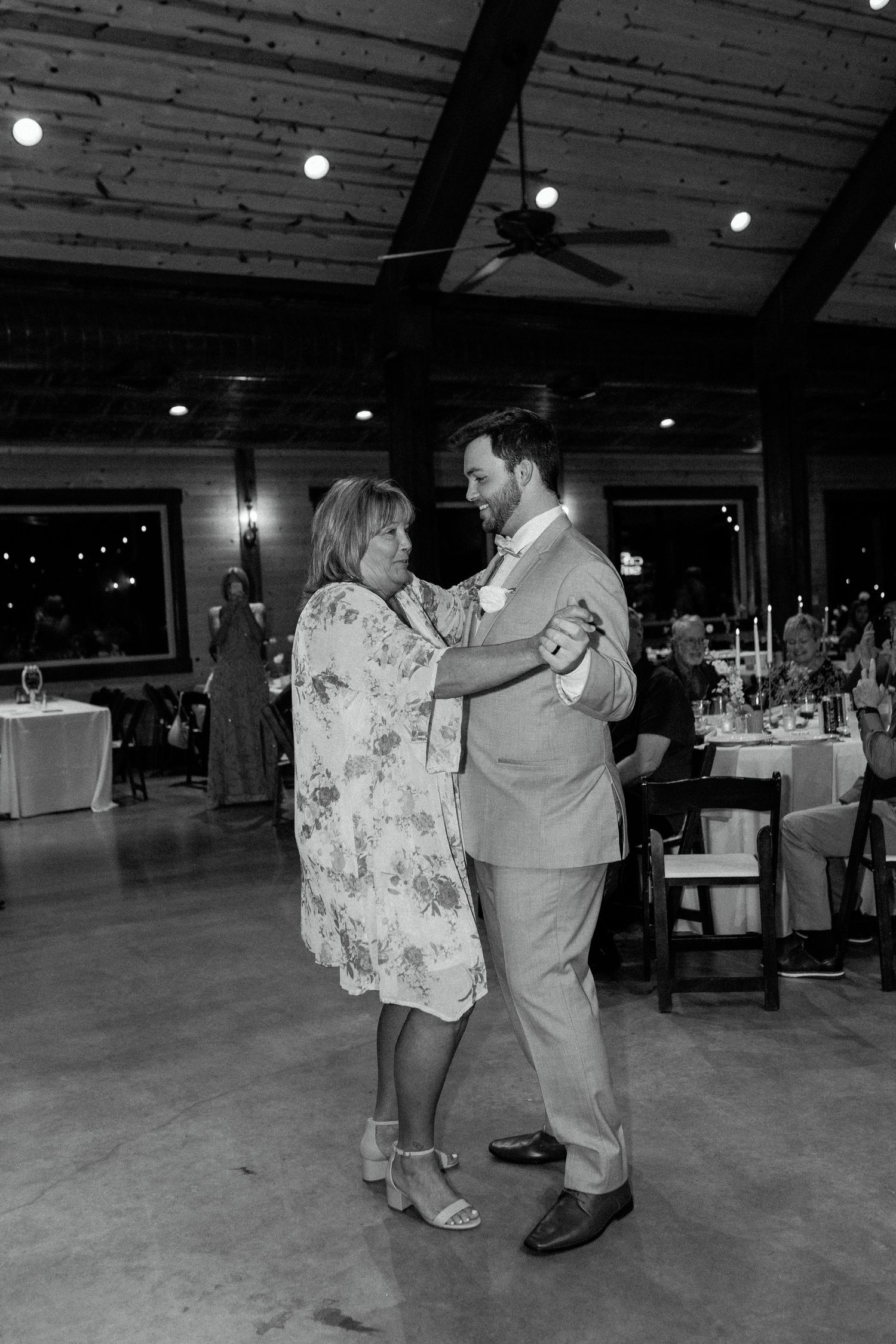 A couple dances together on a dark dance floor at an indoor venue with dim lighting and ceiling beams.