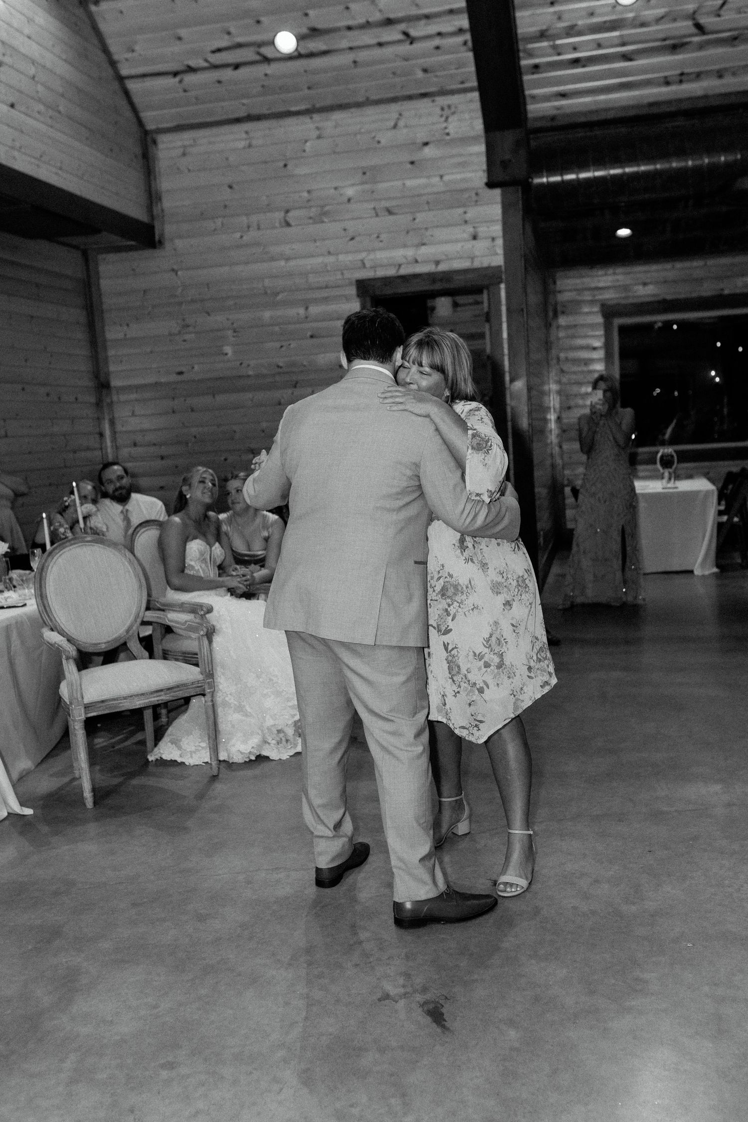 A couple shares an intimate dance moment at a wedding reception in a rustic wooden venue.