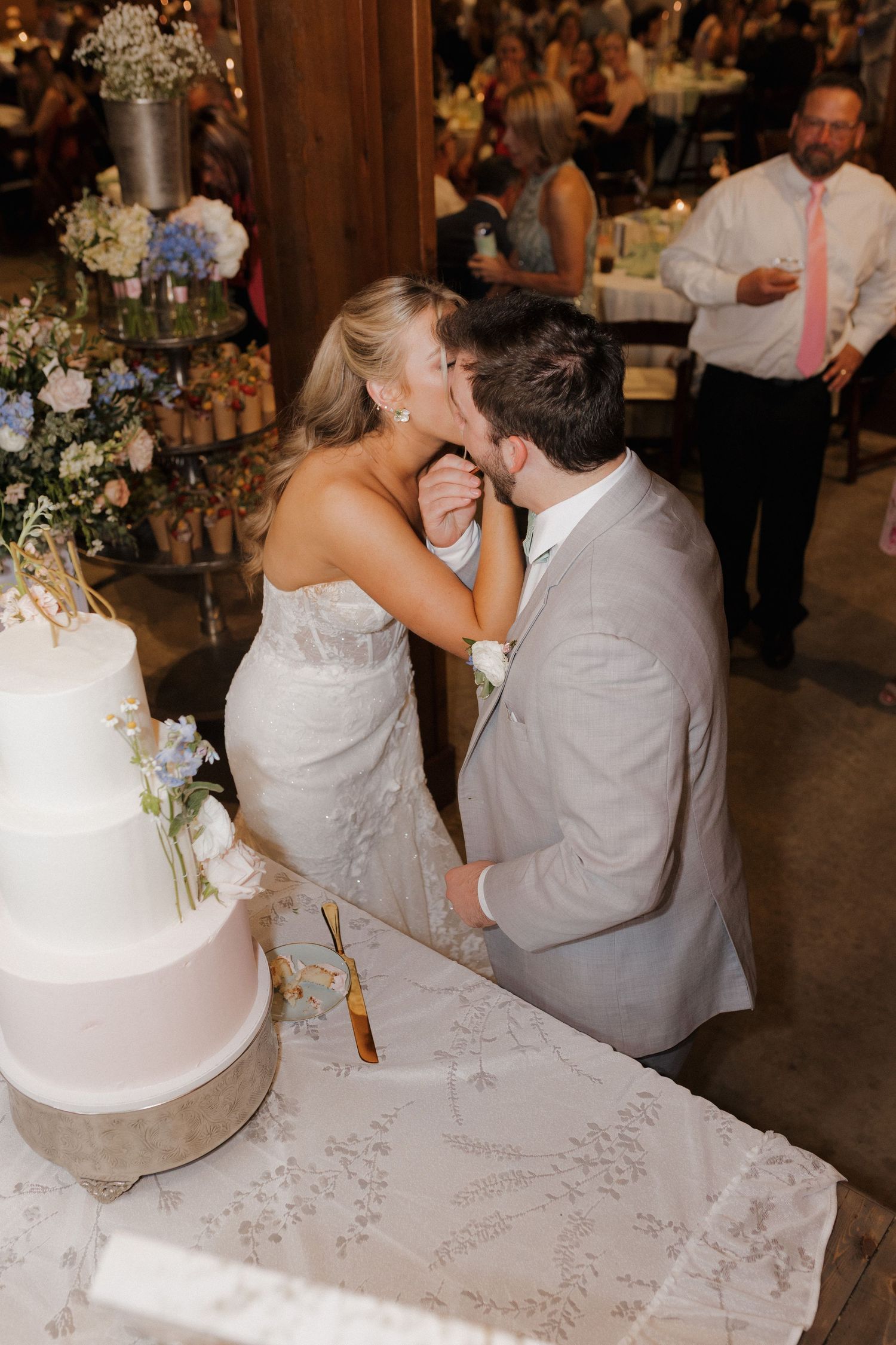 A tender moment between newlyweds sharing cake by their wedding dessert table.