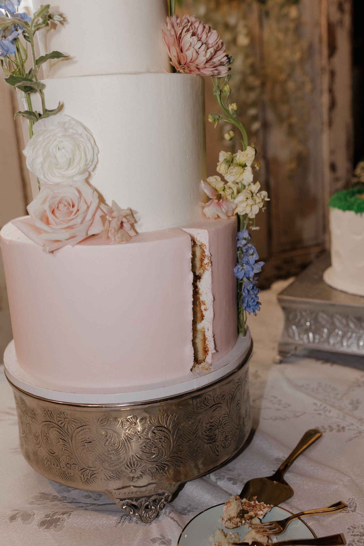 Elegant white and pink wedding cake decorated with fresh flowers on an ornate silver stand.