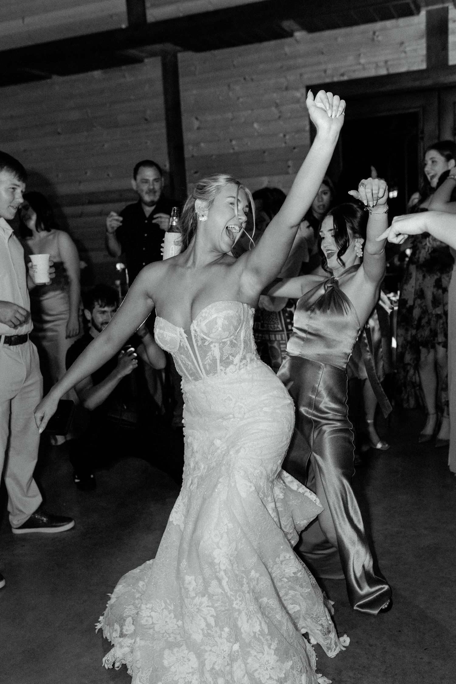 A person in a white lace wedding dress dances joyfully with raised arms on a dance floor during a celebration.