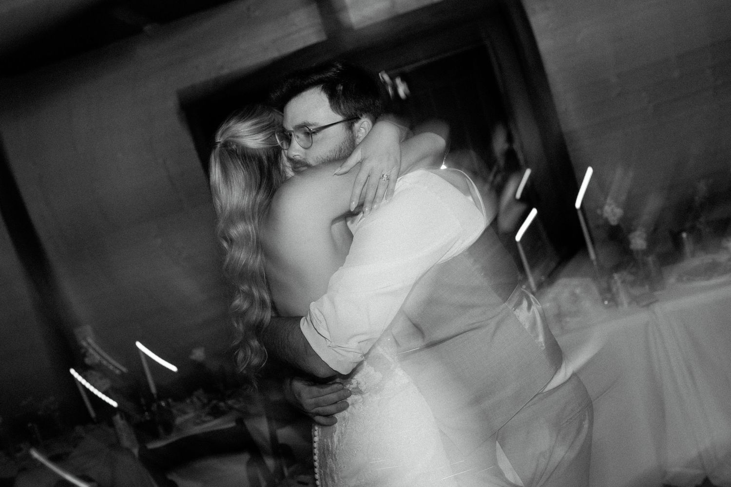 A black and white photo captures a tender kiss between a couple at an intimate wedding reception.