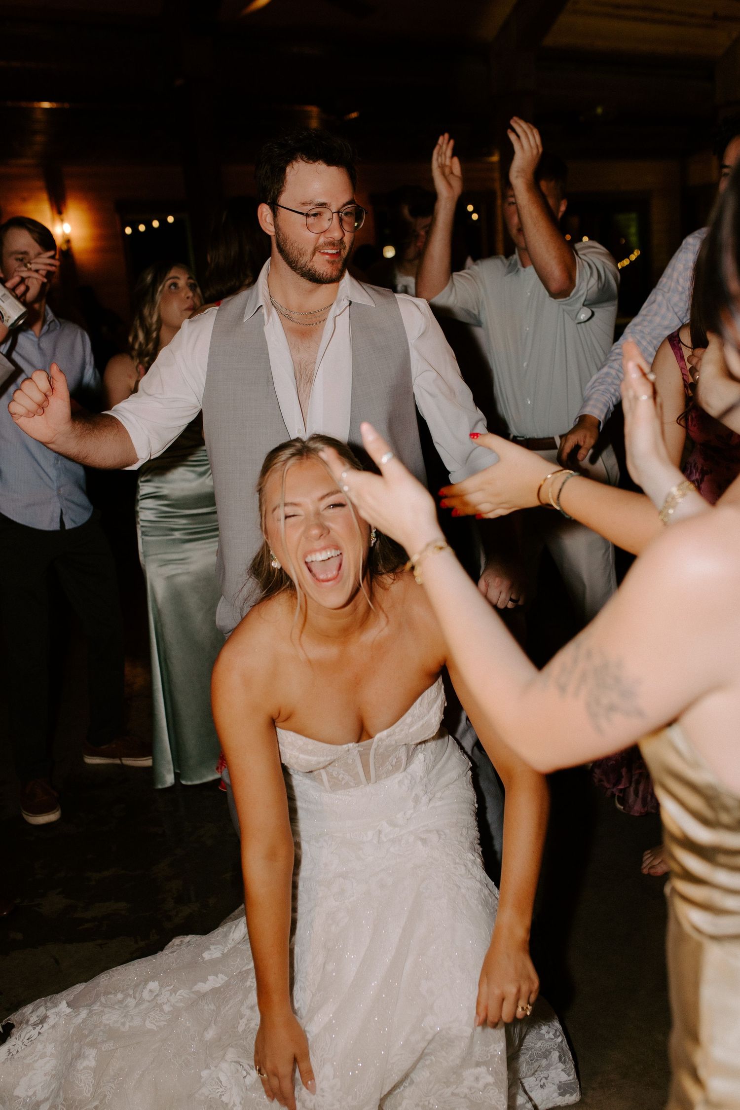 Wedding guests dancing joyfully at a dark reception venue with warm lighting.
