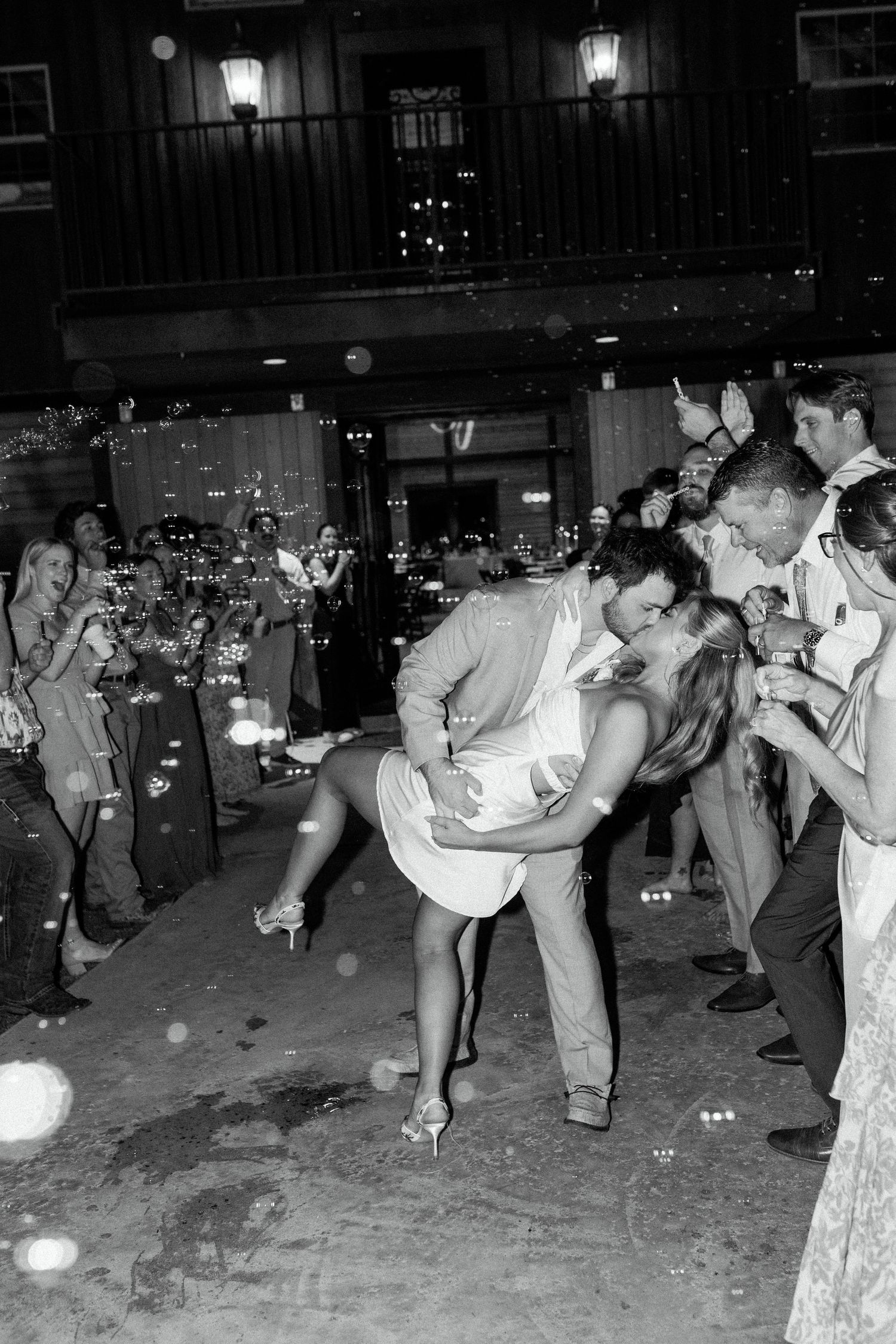 A couple shares a dramatic dip-style dance move while others watch and bubbles float through the festive nighttime scene.
