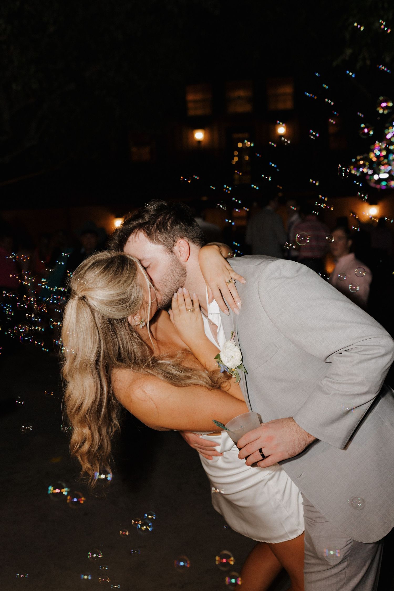 A romantic couple sharing a kiss surrounded by bubbles during a wedding celebration at night.