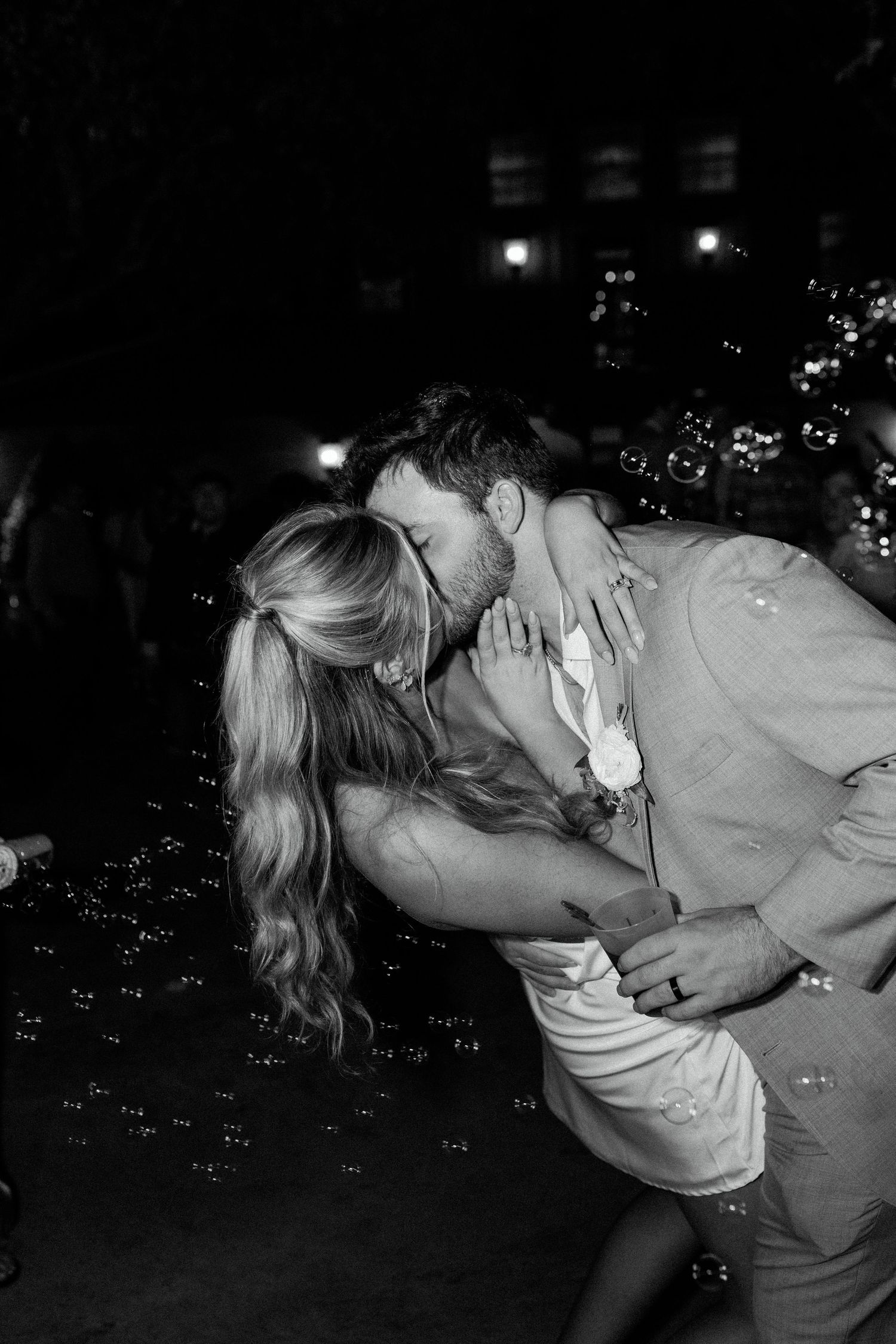 Black and white romantic photo of a couple sharing a passionate kiss with bubbles floating in the dark nighttime background.