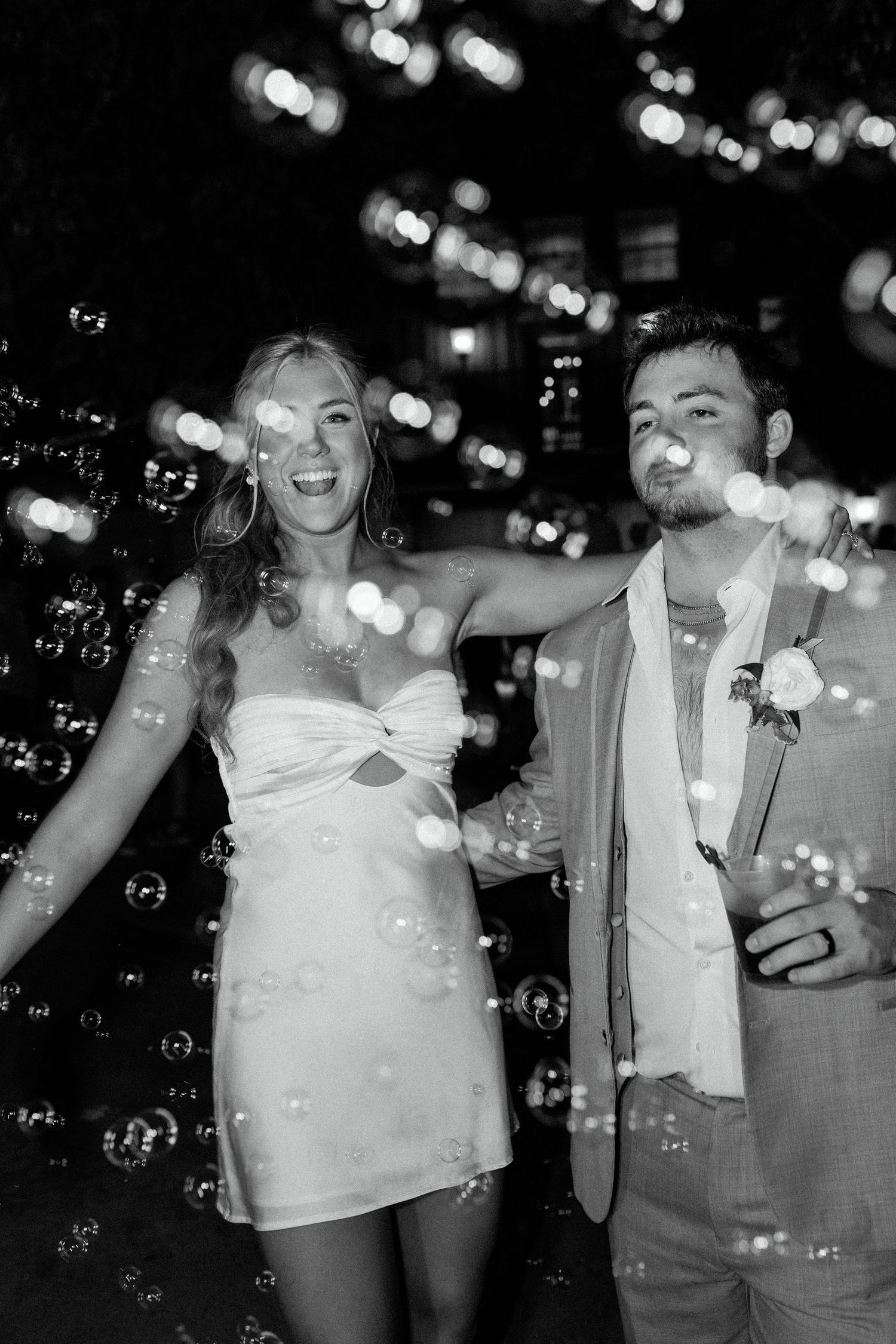 A couple celebrates at a nighttime event surrounded by floating bubbles and bokeh lights.