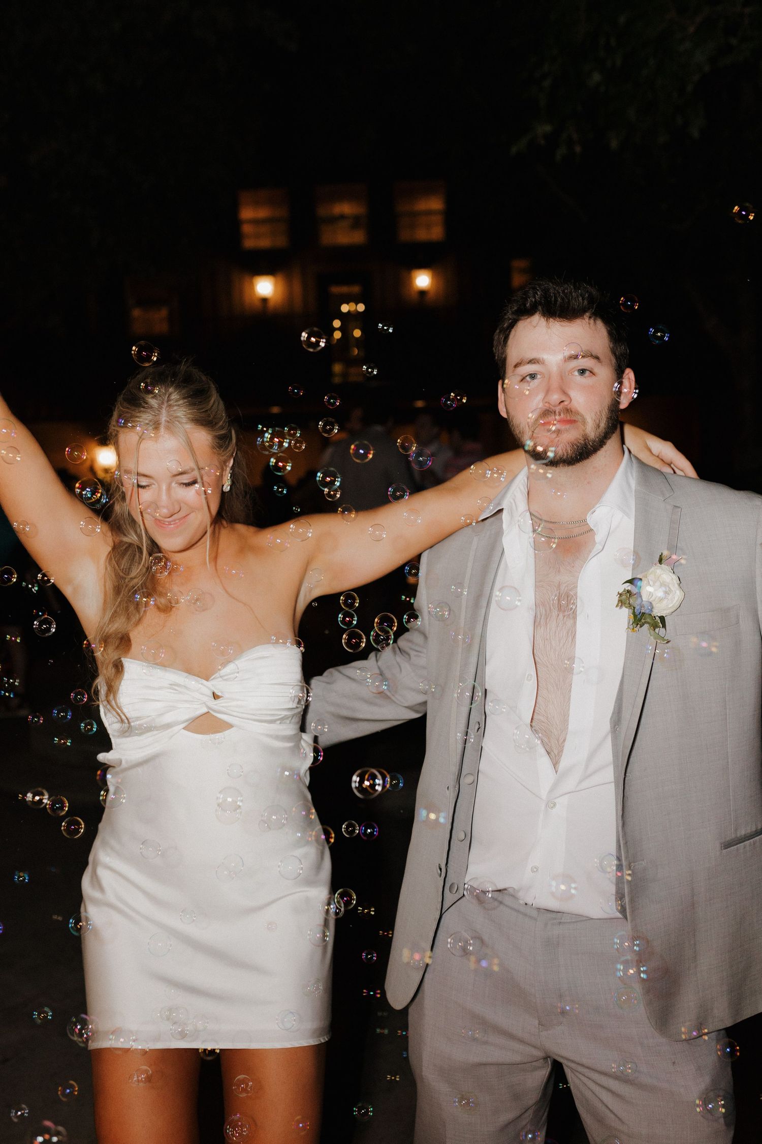 A joyful couple dancing together under floating bubbles at a nighttime celebration with ambient lighting.