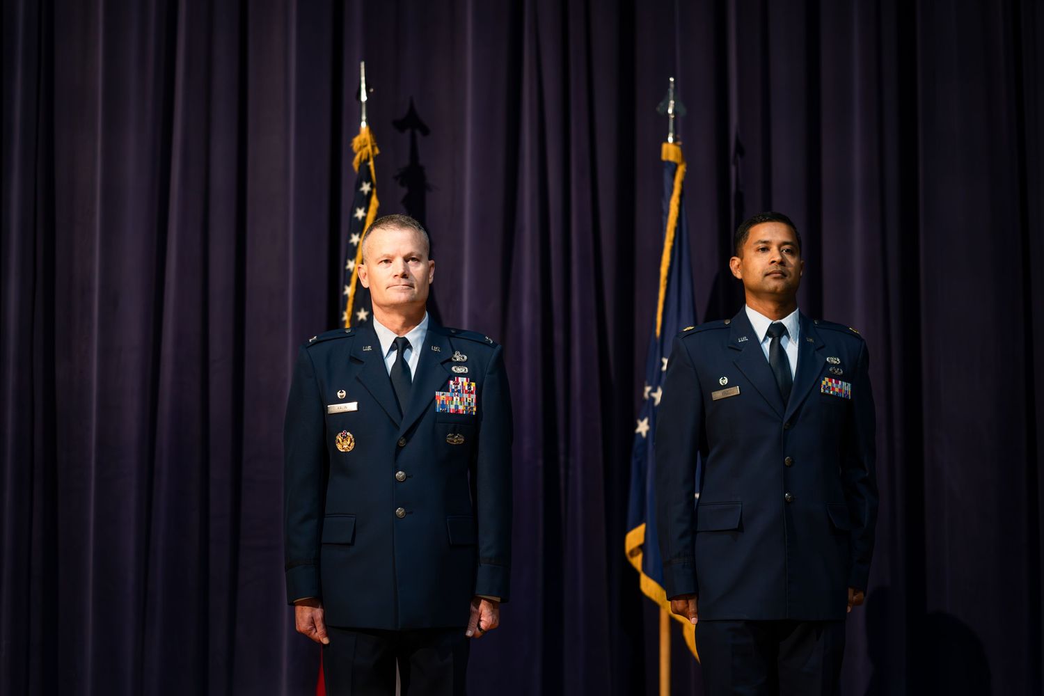 Two military officers in dress blues stand at attention during formal ceremony.