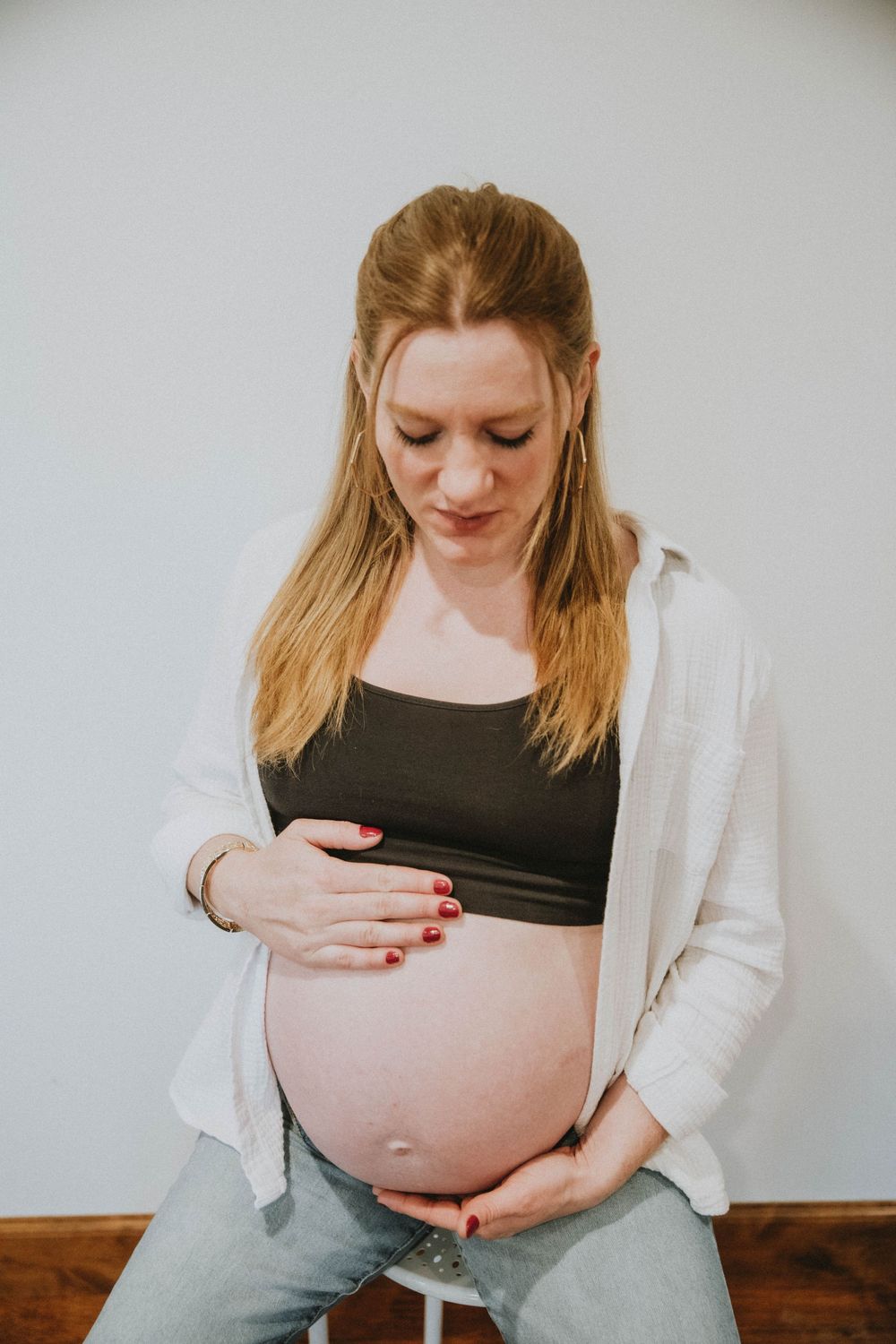 An expectant parent in a white cardigan and gray pants lovingly cradles their pregnant belly while looking down. indiana pa photographer