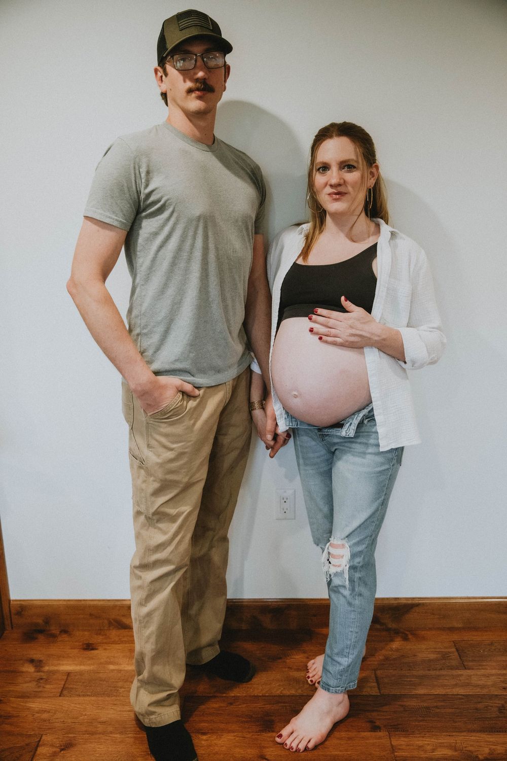Expectant couple standing together on hardwood floor with the pregnant woman wearing a white cardigan indiana pa photographer