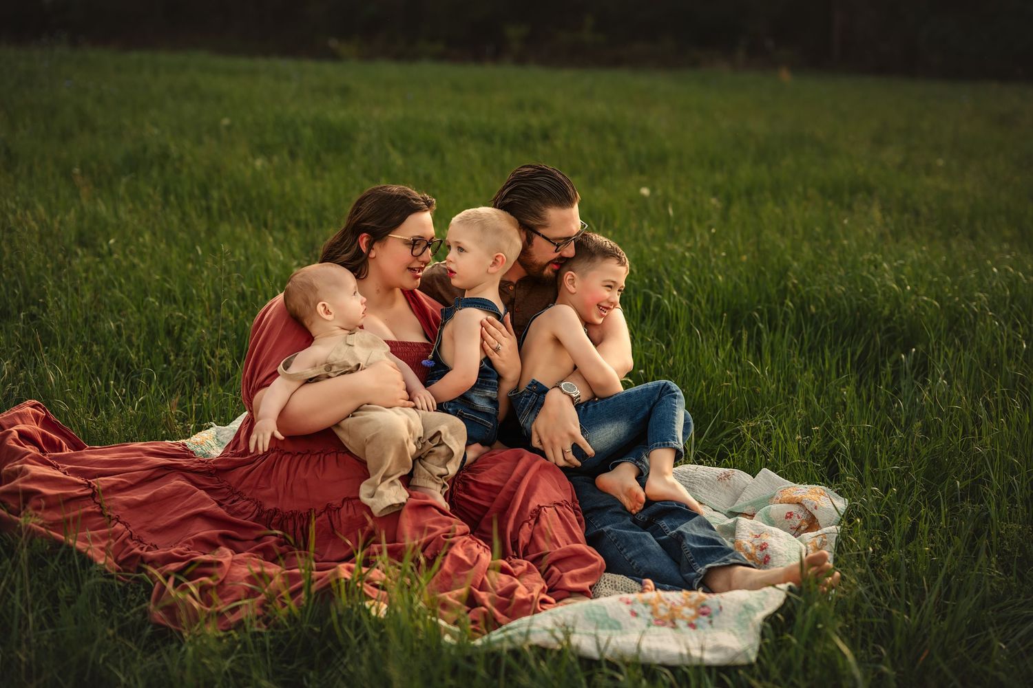 Family enjoying a picnic together on a blanket in a lush green field on a sunny day for family photos.