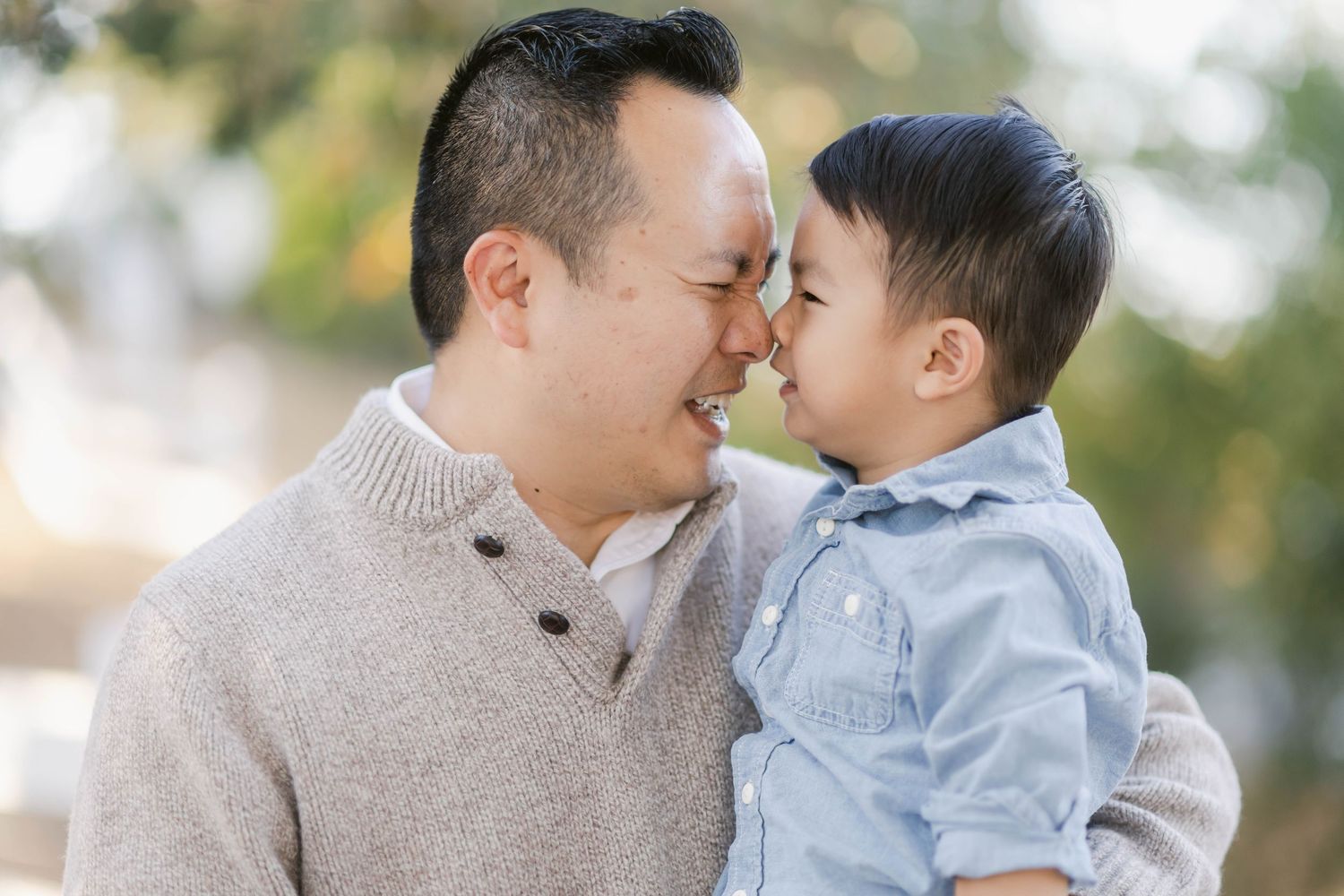 Two people share a tender loving moment outdoors surrounded by soft bokeh lighting in a park-like setting.