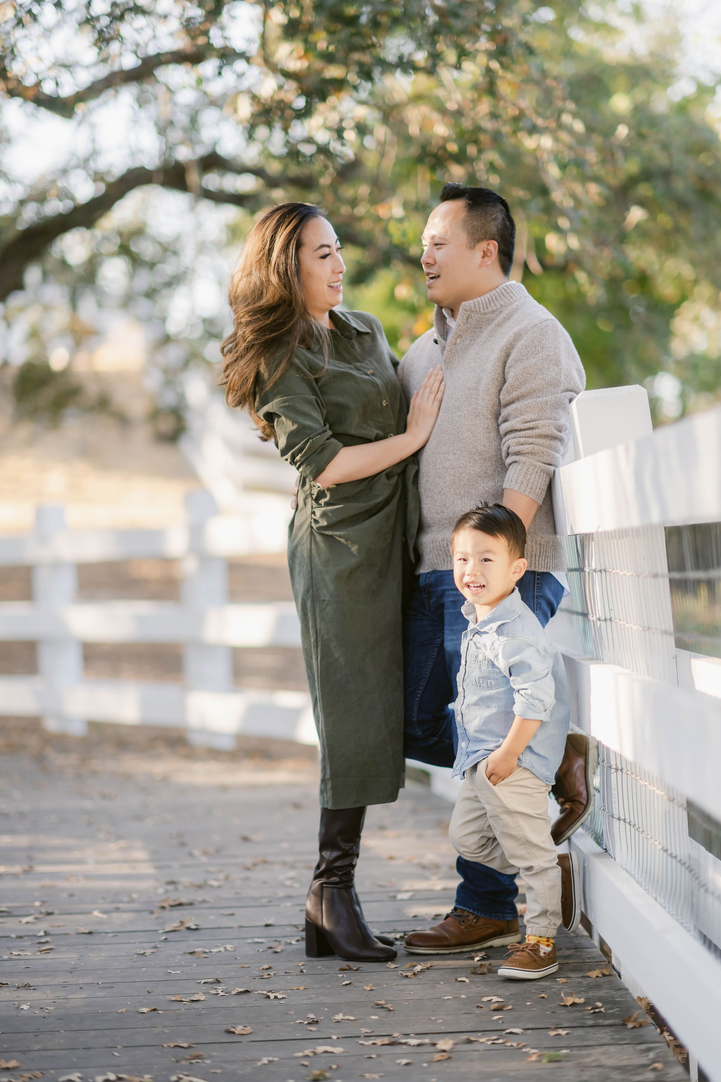 A family shares a joyful moment together while standing along a white wooden fence on an autumn day.