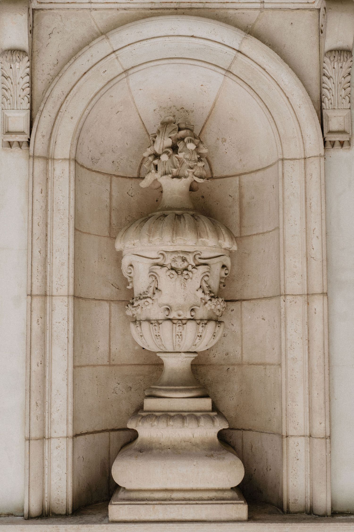 Classical stone urn with ornate carvings set in arched wall niche.