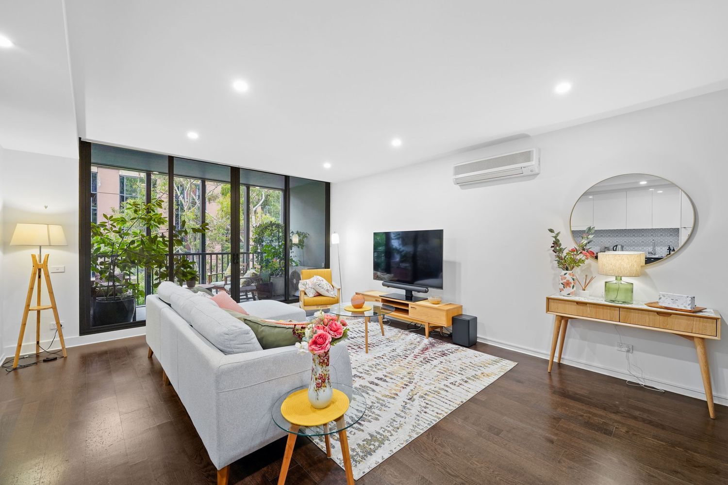 Modern apartment living room with white sofa, dark hardwood floors, floor lamp, and glass sliding doors leading to balcony.