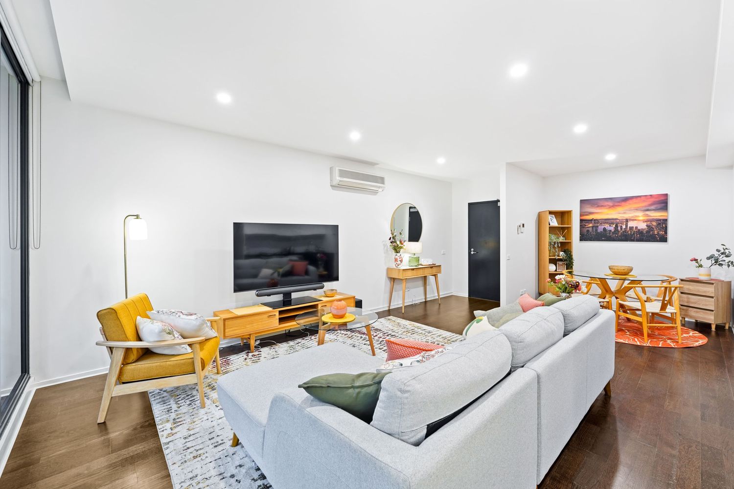 Modern living room with yellow accent chairs, light gray sofa, wooden TV unit, and dark hardwood flooring.