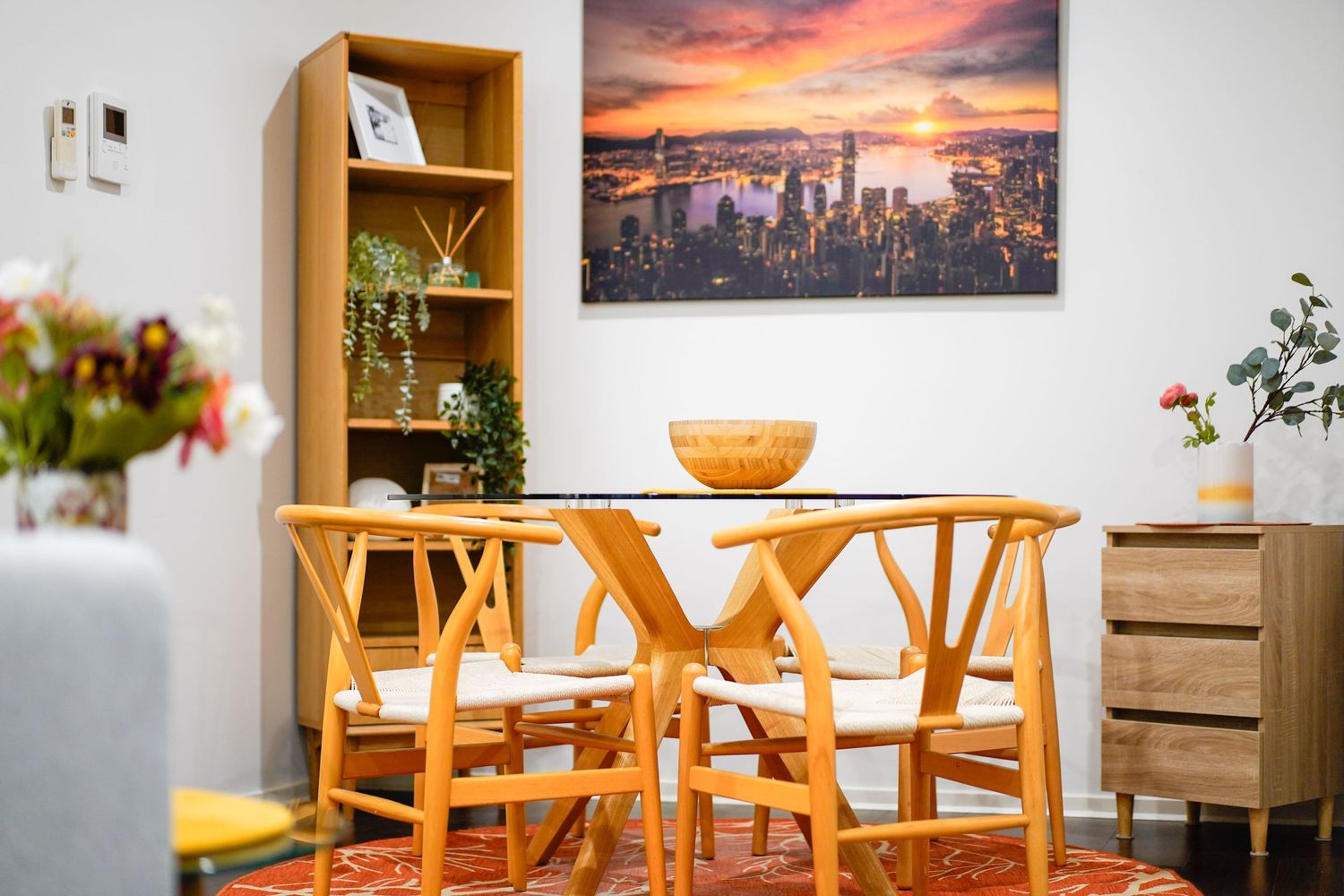 Modern dining area with wooden wishbone chairs, featuring cityscape wall art and orange accents.