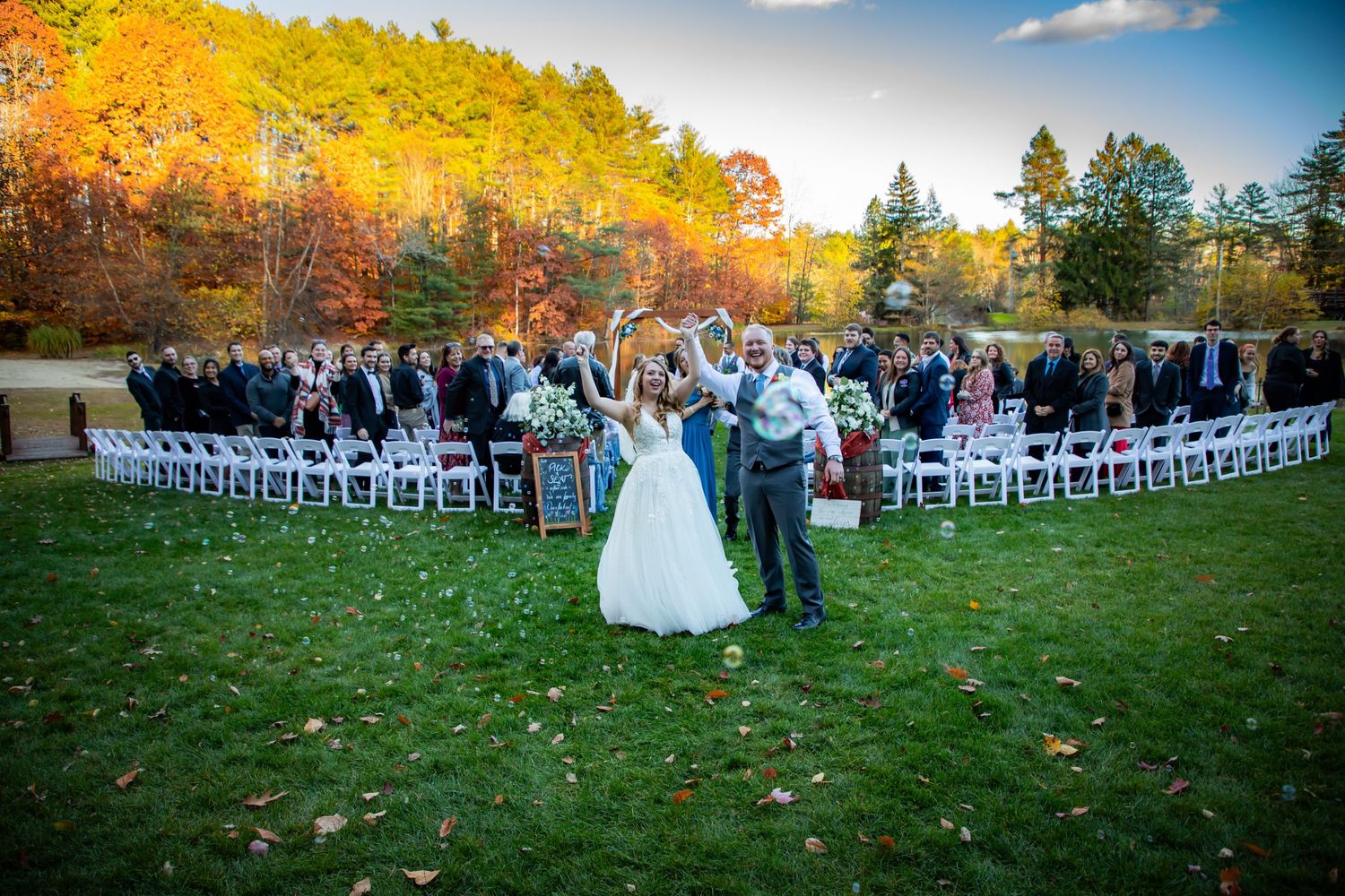 Wedding ceremony taking place on a lawn surrounded by autumn foliage.
